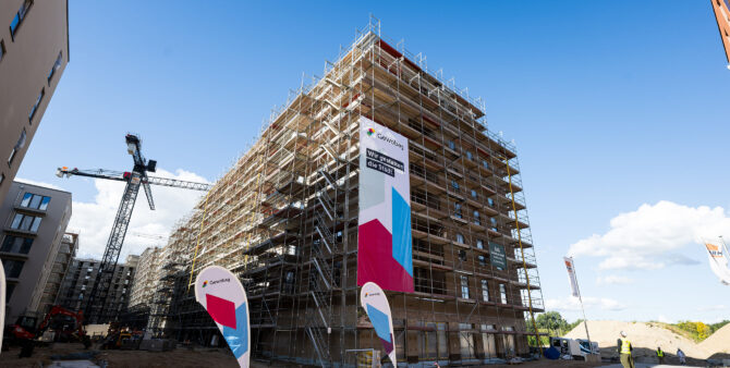 Aus der Froschperspektive: Blick auf einen fast fertigen Rohbau, der noch eingerüstet ist. Am Gerüst hängt ein großes Gewobag-Banner mit der Aufschrift "Wir gestalten die Stadt". Foto: City-Press GmbH