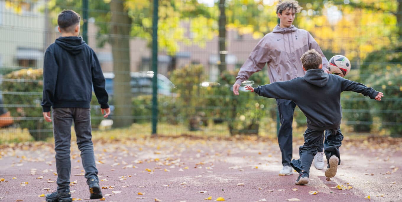 Szene aus einem Fußballkäfig: Ein Kind und ein Jugendlicher spielen sich den Ball zu, ein weiteres Kind steht daneben und schaut zu. Foto: Felix Seyfert