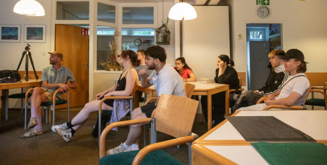 Momentaufnahme aus einem Workshop: Schülerinnen und Schüler im Teenageralter sitzen in einem Raum an Tischen und schauen in eine Richtung. Foto: Ludger Paffrath