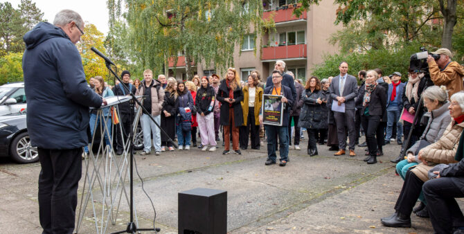 Eine Gruppe von Menschen steht bei einer Veranstaltung in einem Wohnquartier im Kreis und hört einem Redner zu. Foto: Ludger Paffrath