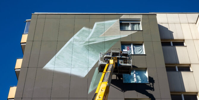 Großaufnahme: Die Fassade eines Hochhauses wird von einem Kran-Arm aus bemalt. Foto: Ludger Paffrath