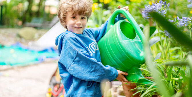 Ein Junge gießt Pflanzen mit einer grünen Gießkanne. Foto: Ralph Maak