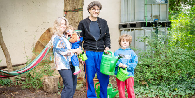 Ein Mann, eine Frau und zwei Kinder posieren mit Gießkannen in der Hand in einem begrünten Innenhof und lächeln in die Kamera. Im Hintergrund ist eine Regentonne zu sehen. Foto: Ralph Maak