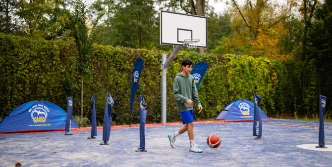 Szene von einem Basketballplatz im Freien: Ein Junge dribbelt einen Basketball, um ihn herum sind Slalomstangen aufgebaut. Foto: City-Press GmbH