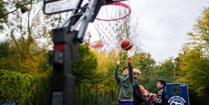 Szene von einem Basketballplatz im Freien: Ein Junge wirft einen Basketball auf einen Korb. Foto: City-Press GmbH