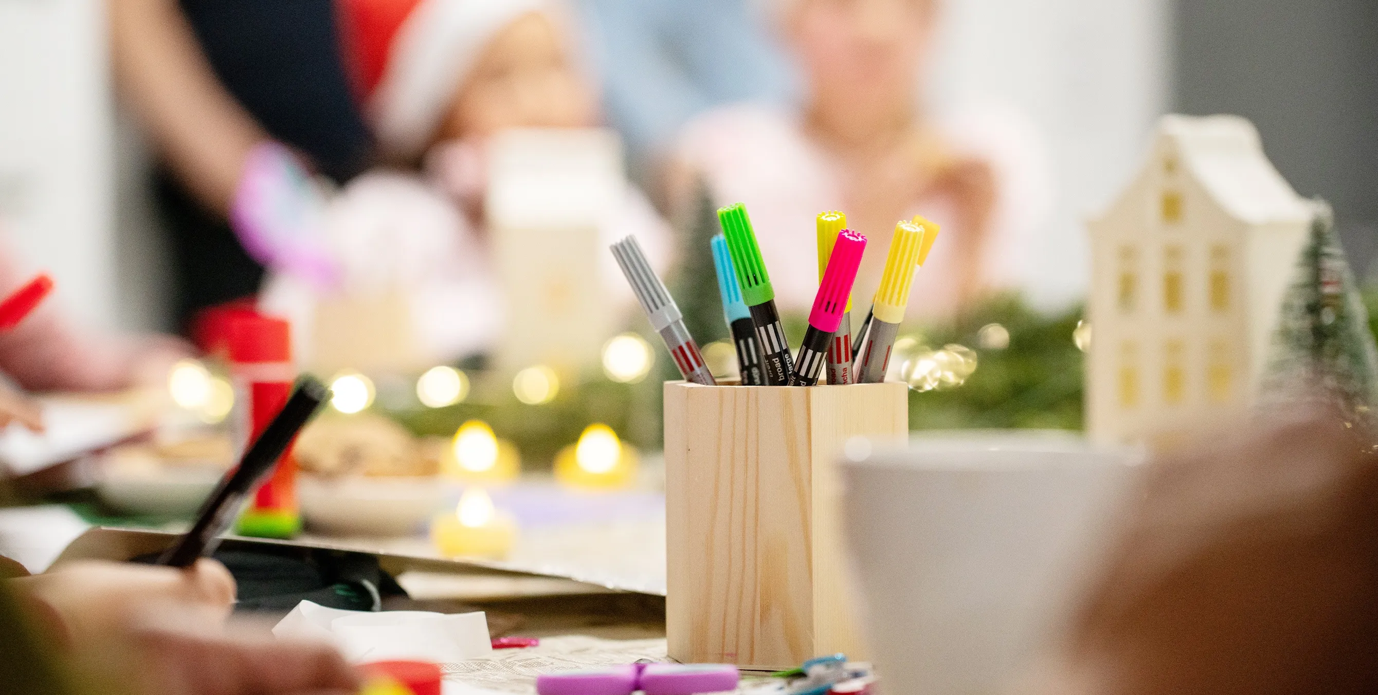 Großaufnahme: ein mit Filzstiften gefüllter Holzbecher auf einem weihnachtlich dekorierten Tisch. Foto: Ralph Maak