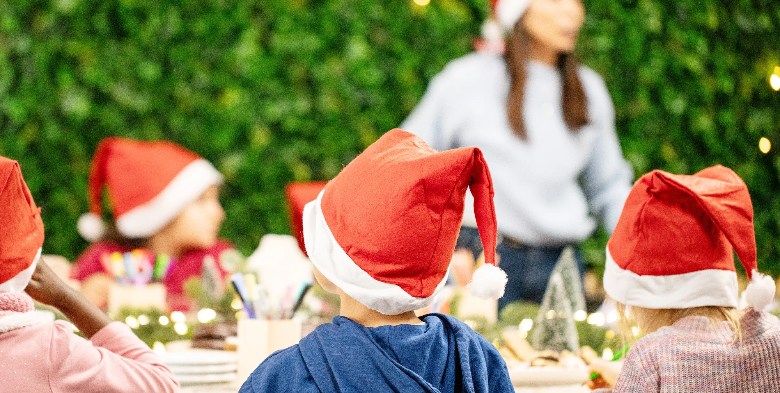 Eine Gruppe Kinder mit Weihnachtmützen auf dem Kopf sitzt an einem weihnachtlich geschmückten Tisch und malt. Foto: Ralph Maak