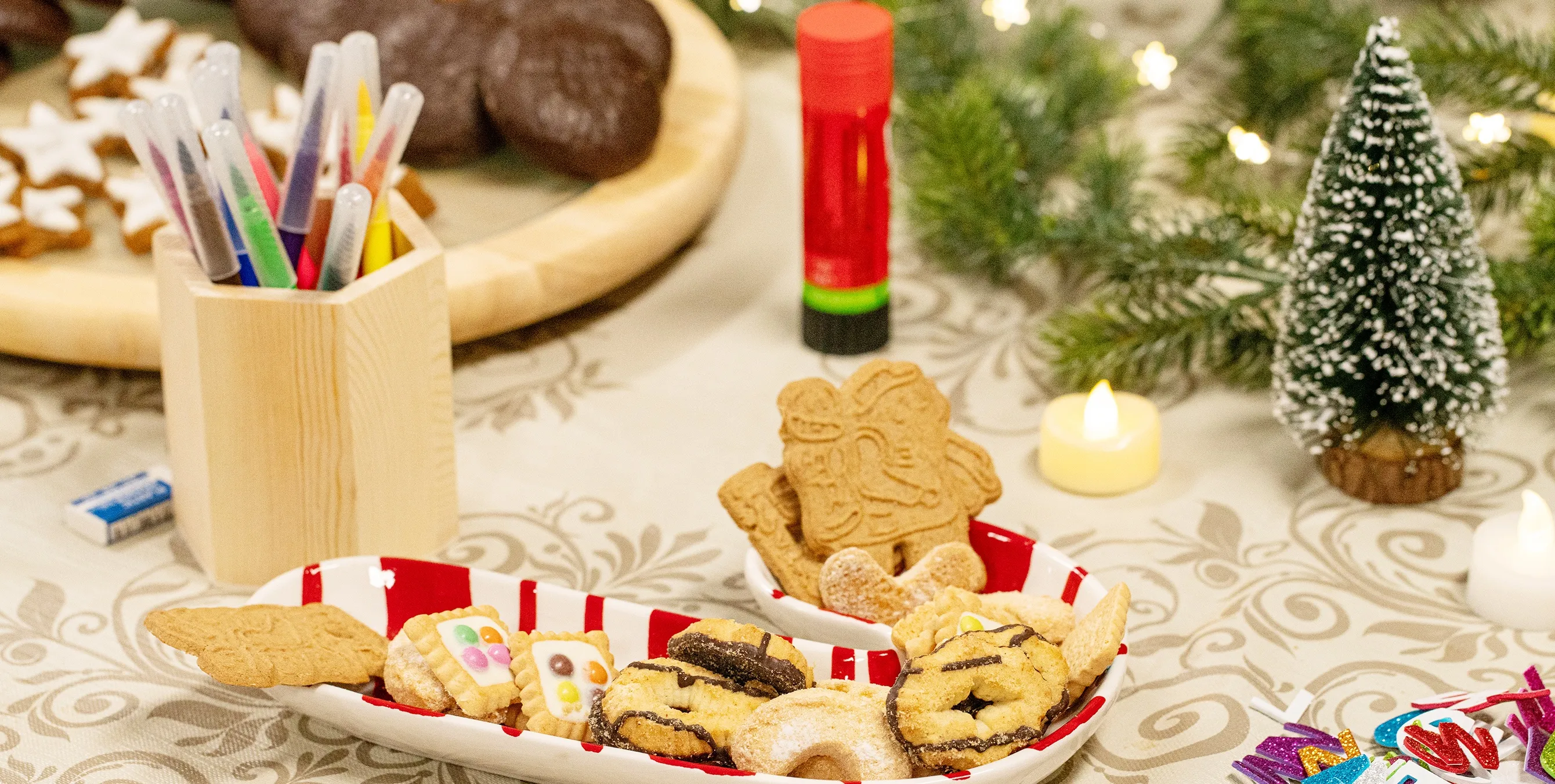 Großaufnahme: ein weihnachtlich dekorierter Tisch mit Weihnachtsgebäck, Filzstiften, Klebebuchstaben und einem Klebestift. Foto: Ralph Maak