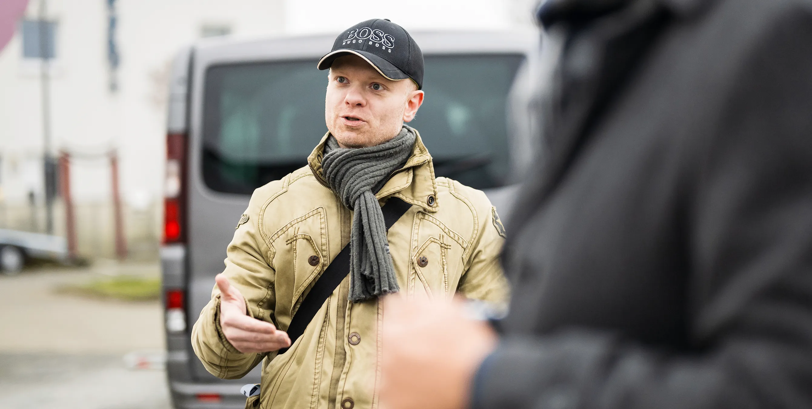 Ein Mann mit Basecap und Schaul steht in einem Wohnquartier und spricht zu einer anderen Person. Foto: City-Press GmbH