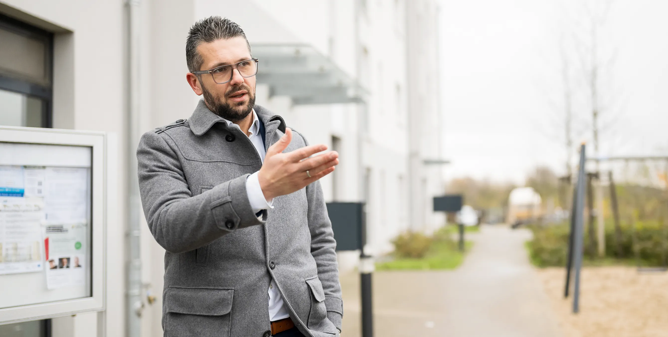 Ein Mann mit Brille steht vor einem Mehrfamilienhaus und spricht gestikulierend. Foto: City-Press GmbH