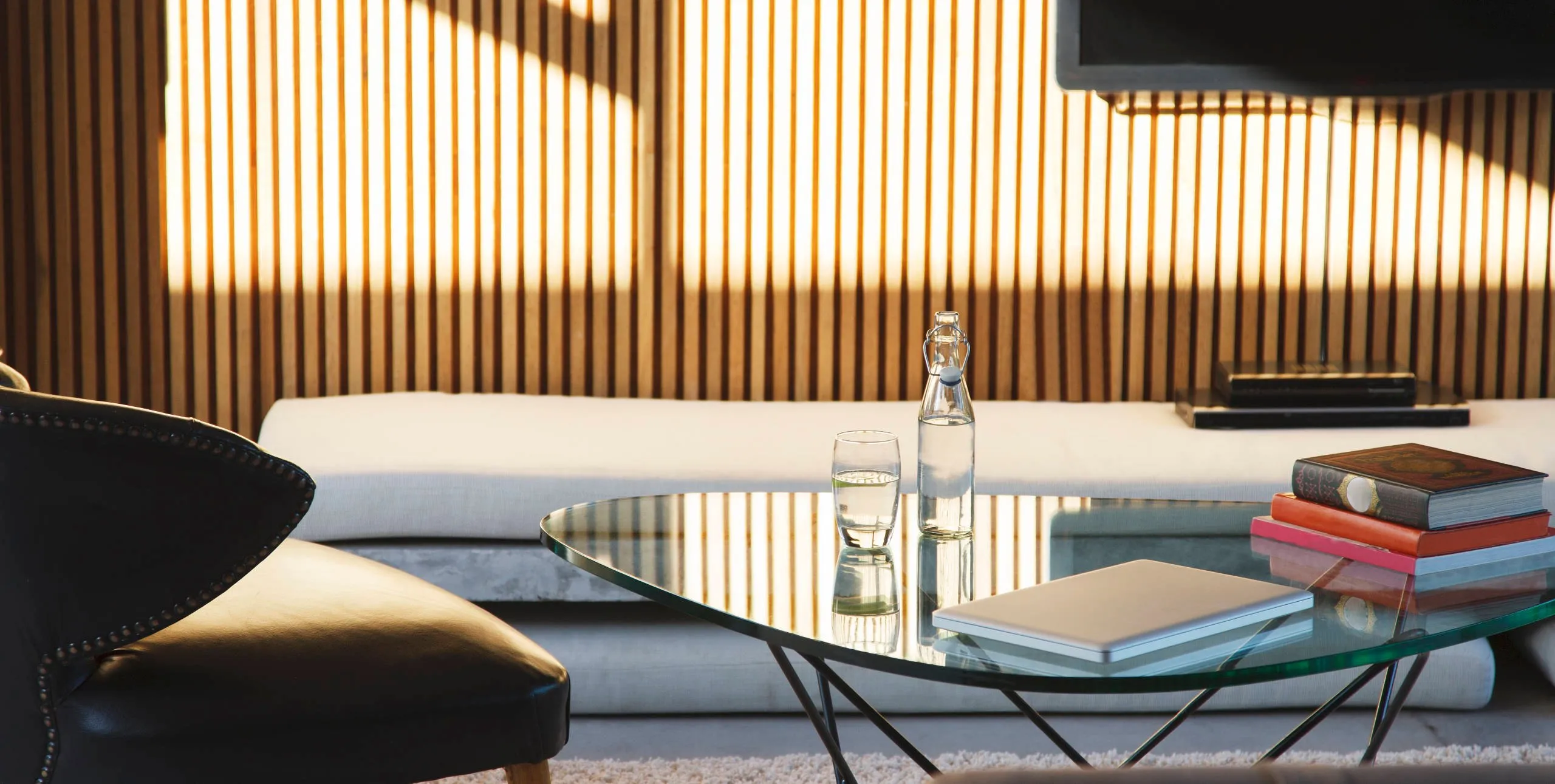 Helles, modernes Wohnzimmer mit Glastisch, schwarzem Sessel, langem Sofa und holvertäfelter Wand