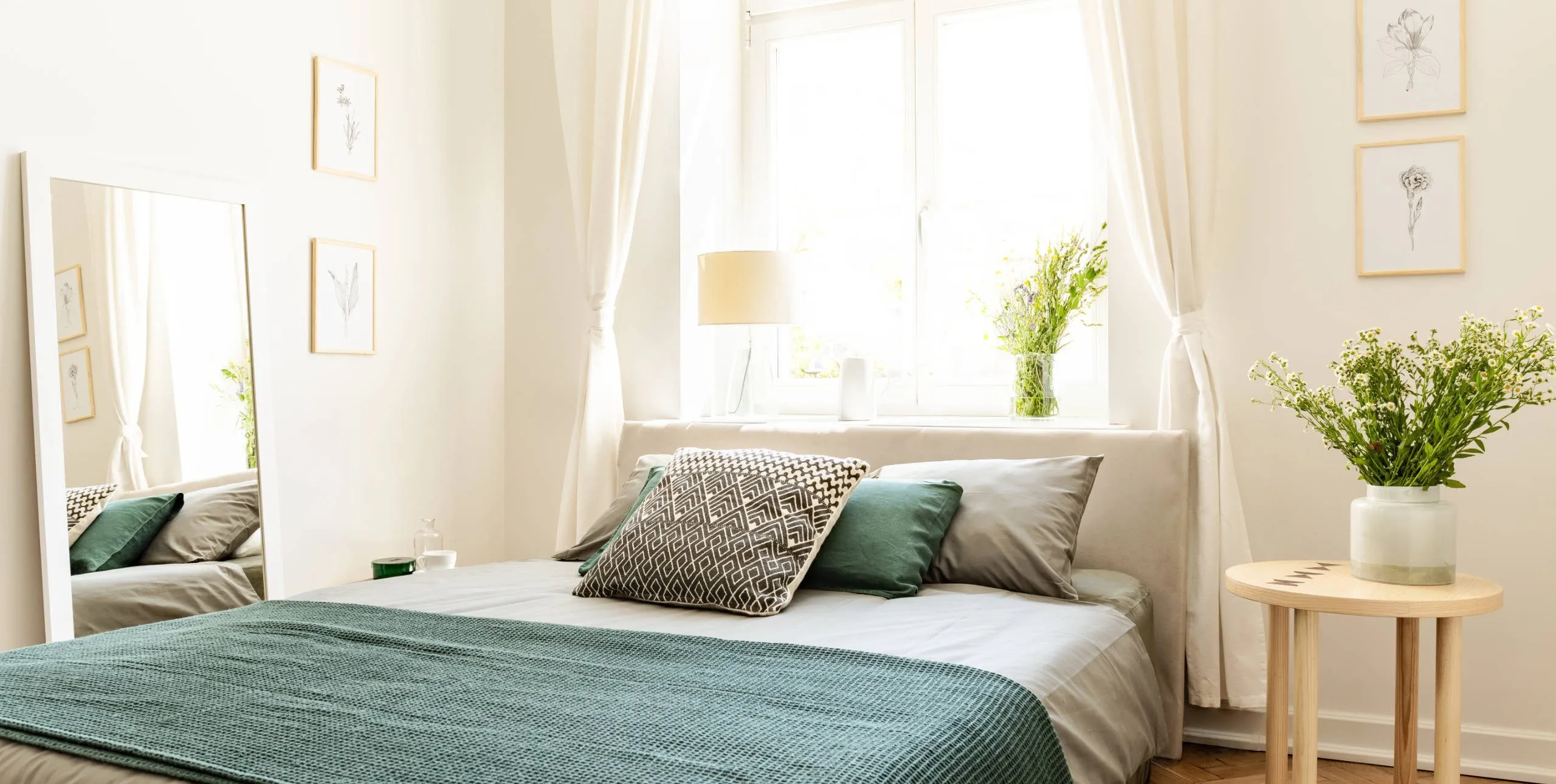Geräumiges, helles Schlafzimmer mit gemachtem Bett, Nachttisch, Blumenvase und großem Spiegel