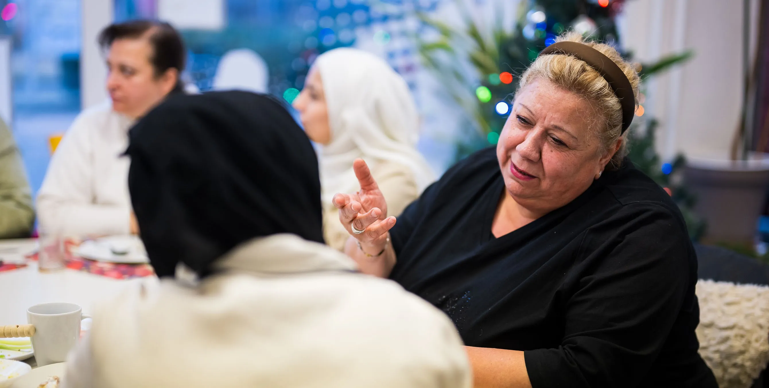 Eine ältere Dame sitzt gemeinsam mit jüngeren, kopftuchtragenden Frauen an einem Tisch und erzählt etwas. Foto: City-Press GmbH