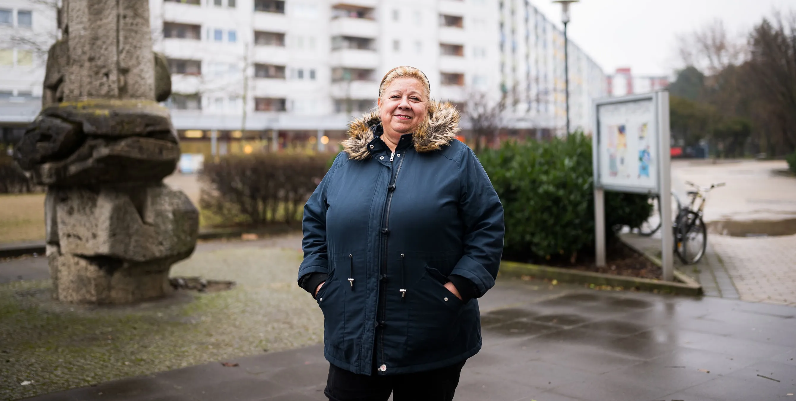 Eine ältere Dame steht in Winterjacke im Freien und lächelt in die Kamera. Im Hintergrund ist ein Wohnblock zu sehen. Foto: City-Press GmbH