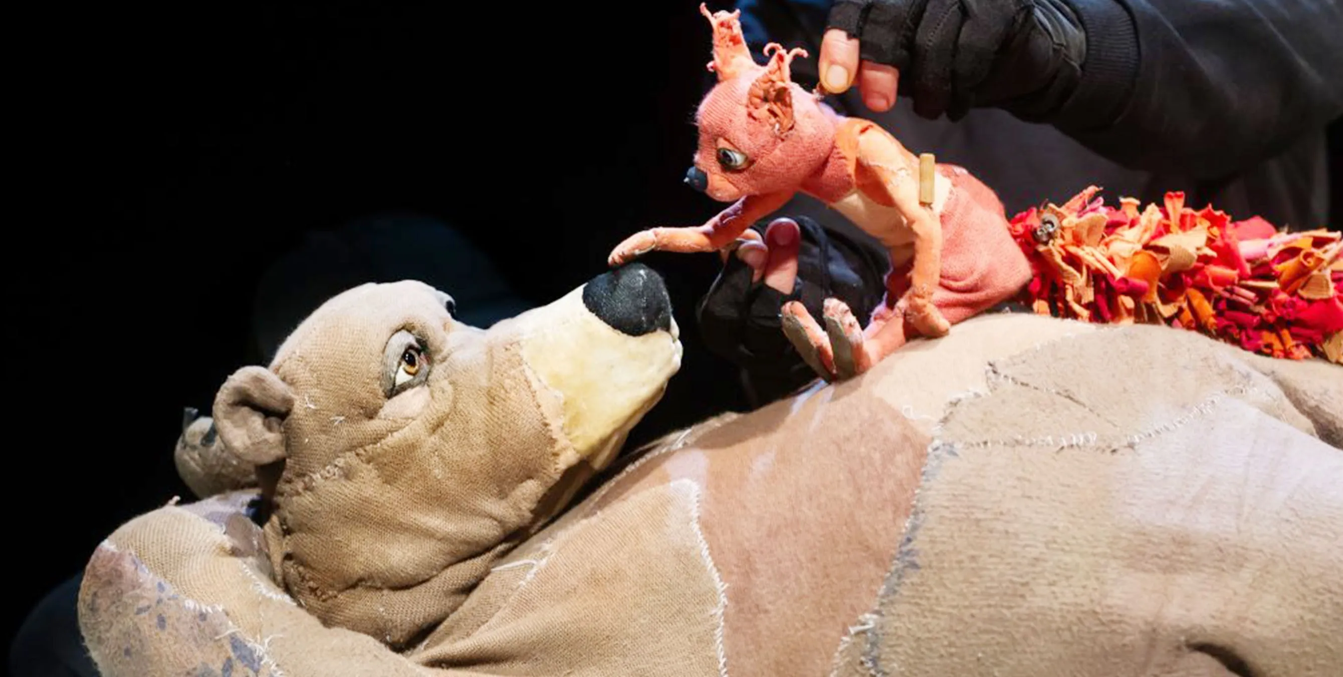 Eine große Bären-Puppe liegt auf dem Rücken. Auf seinem Bauch sitzt eine Eichhörnchen-Puppe und unterhält sich mit ihm. Ebenfalls im Bild: die Finger eines Puppenspielers. Foto: Schaubude