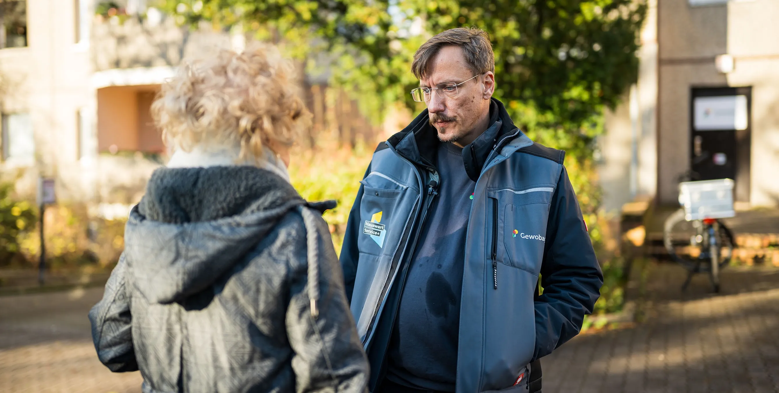 Ein Hauswart steht vor einem Haus und unterhält sich mit einer Frau. Foto: City-Press GmbH