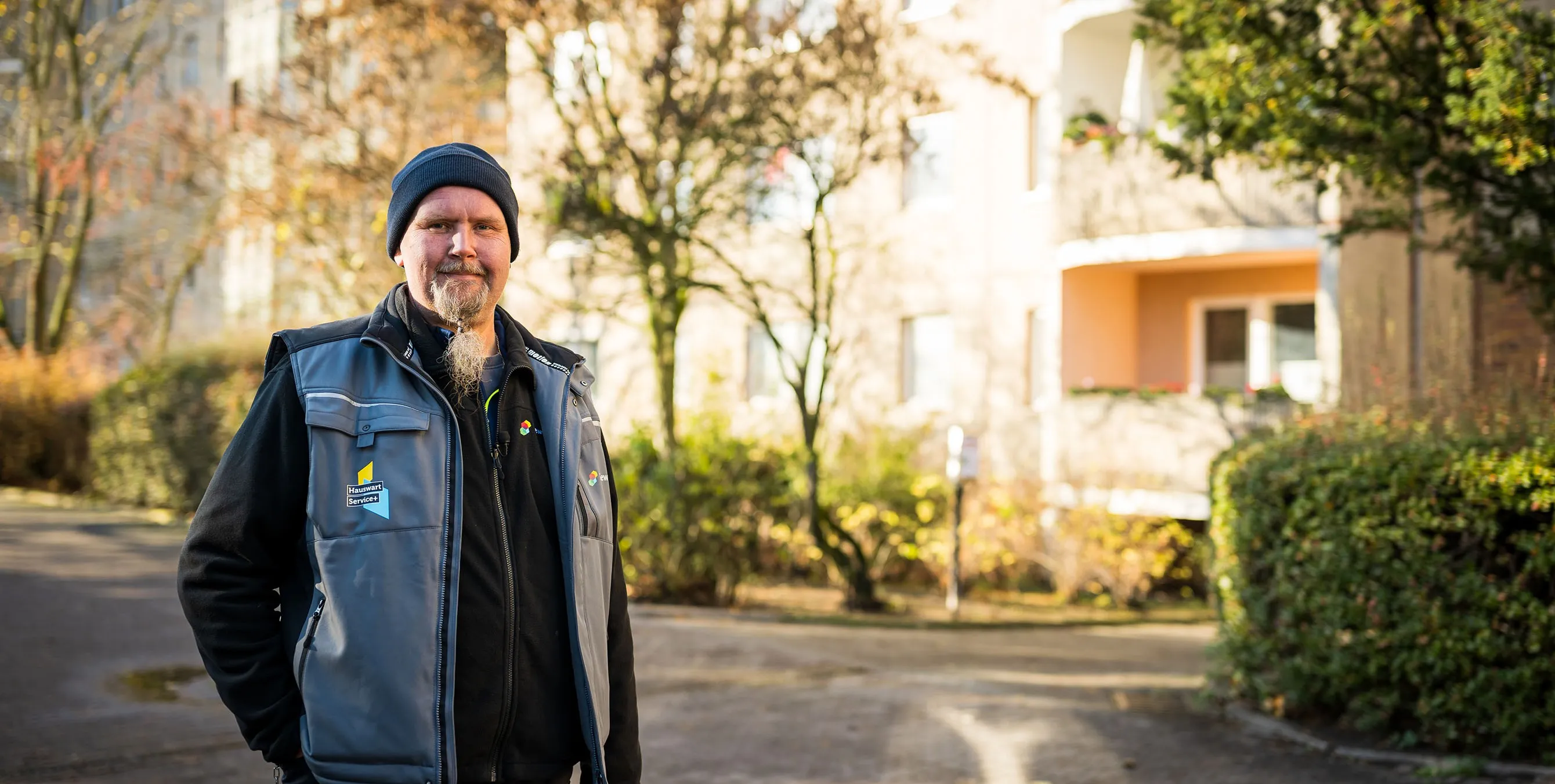 Ein Hauswart steht im Freien vor einem großen Haus und lächelt in die Kamera. Foto: City-Press GmbH