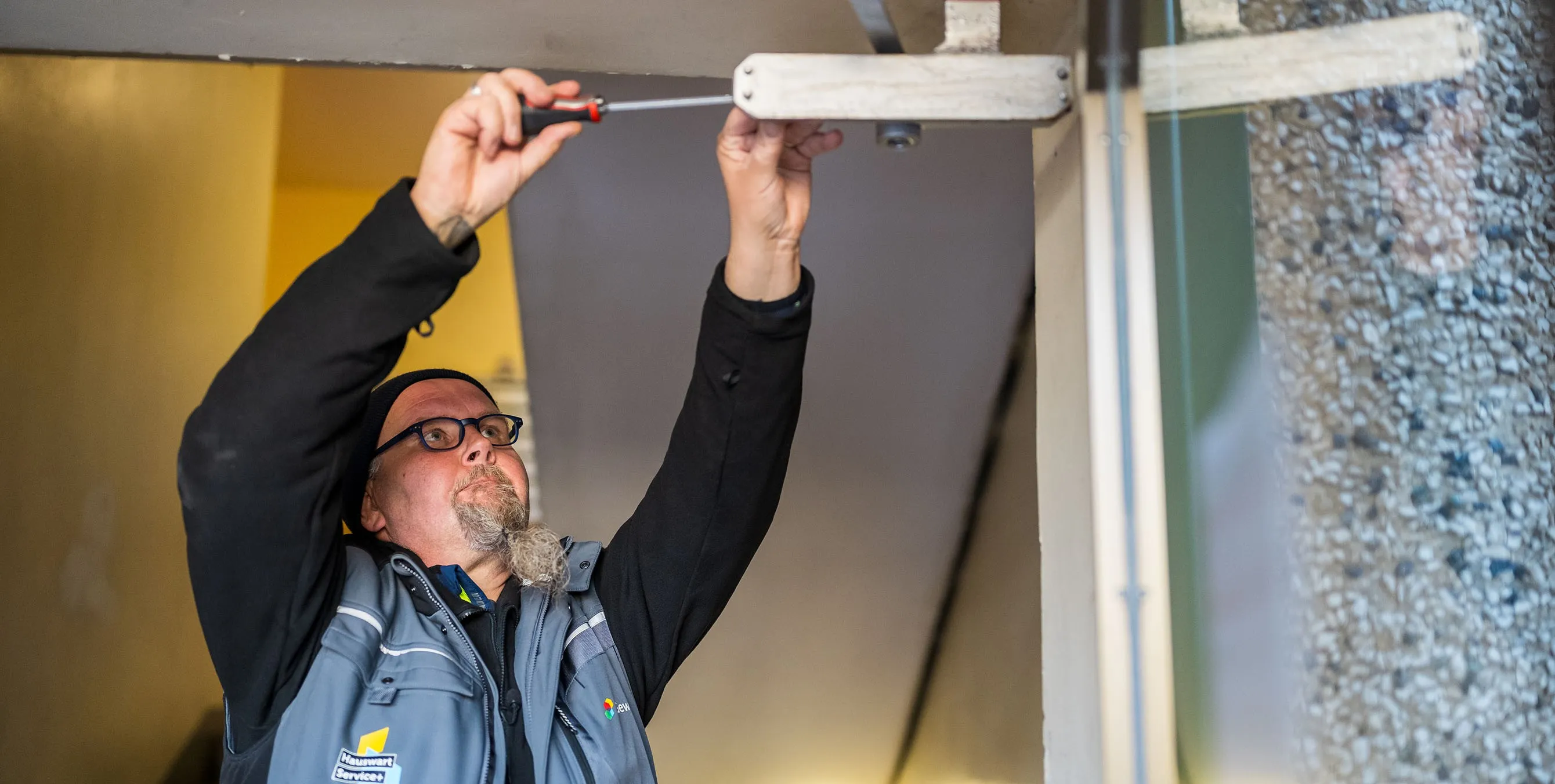 Ein Hauswart arbeitet mit einem Schraubendreher an der Schließmechanik einer Haustür. Foto: City-Press GmbH
