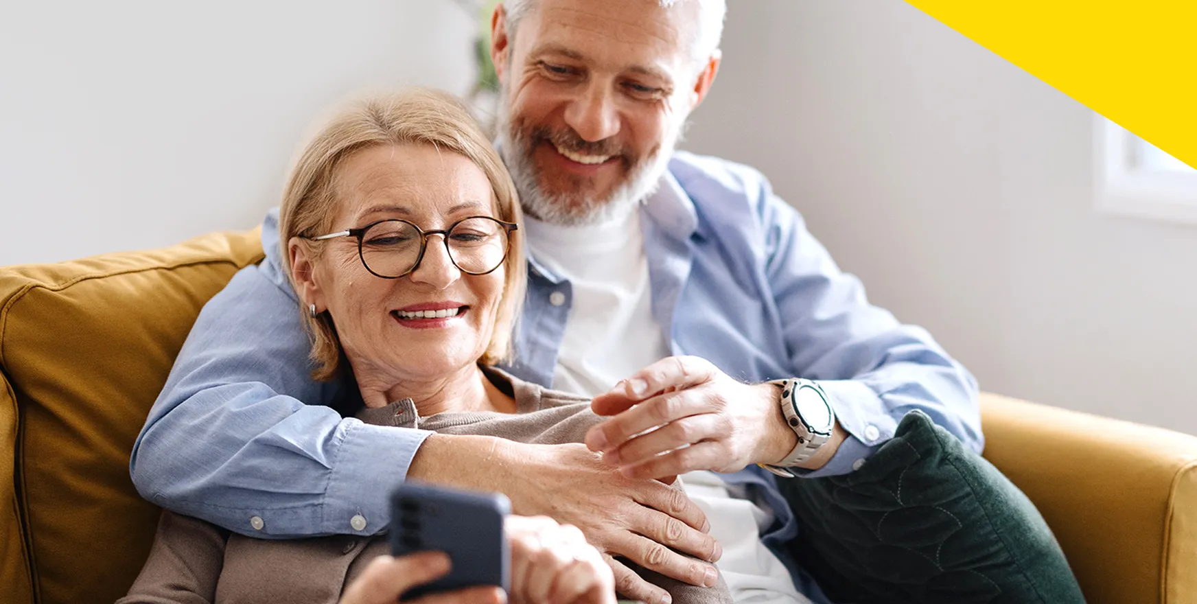 Ein älteres Paar sitz zusammen in einem Ledersessel, lächelt und schaut gemeinsam auf ein Smartphone. Foto: iStock