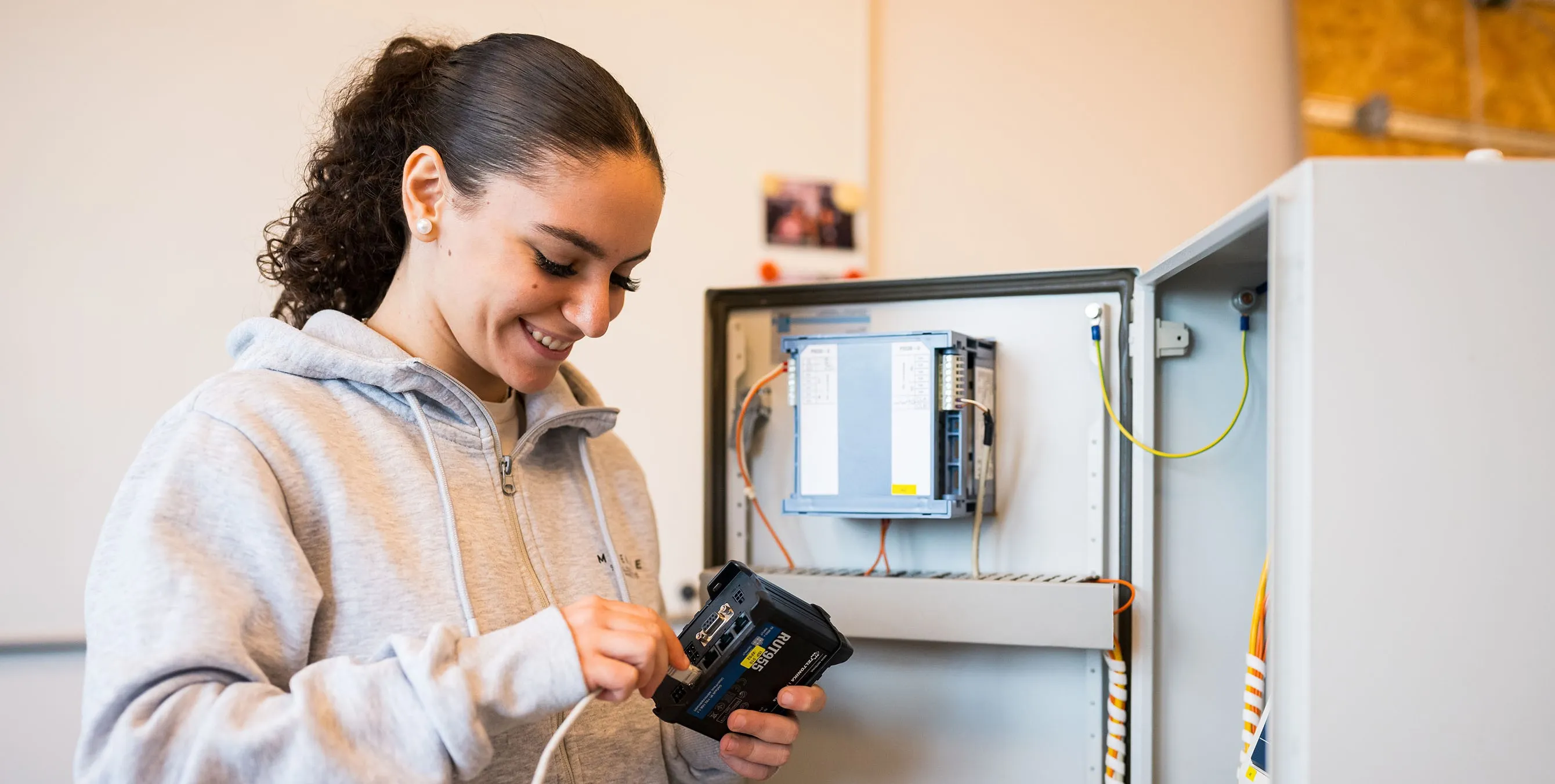 Eine junge Frau steht vor einem Schaltkasten und schließt ein technisches Gerät an. Foto: City-Press GmbH