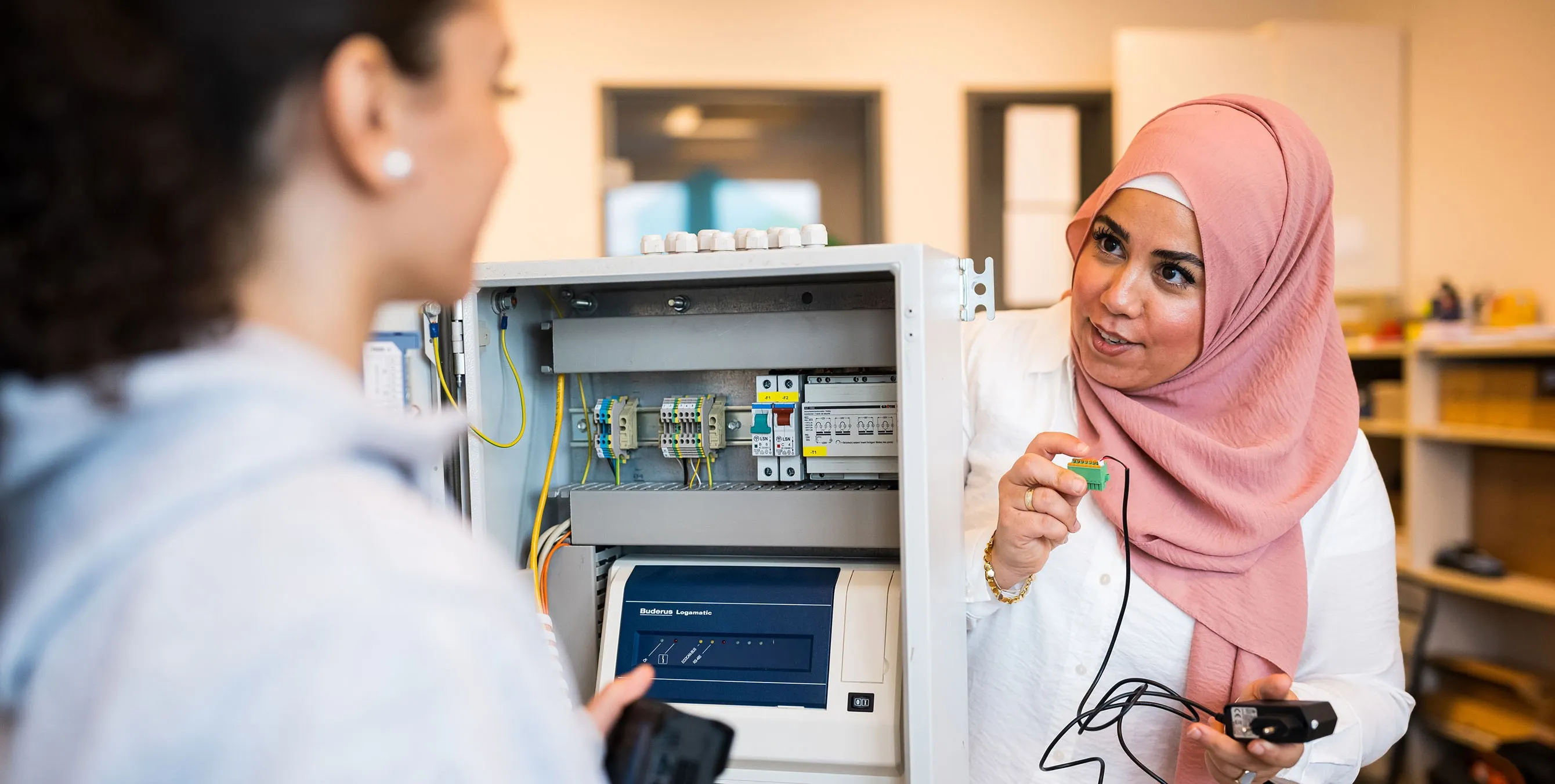 Eine Frau mit Kopftuch steht an einem Schaltkasten, hält ein Kabel in der Hand und scheint einer zweiten Person etwas zu erklären. Foto: City-Press GmbH