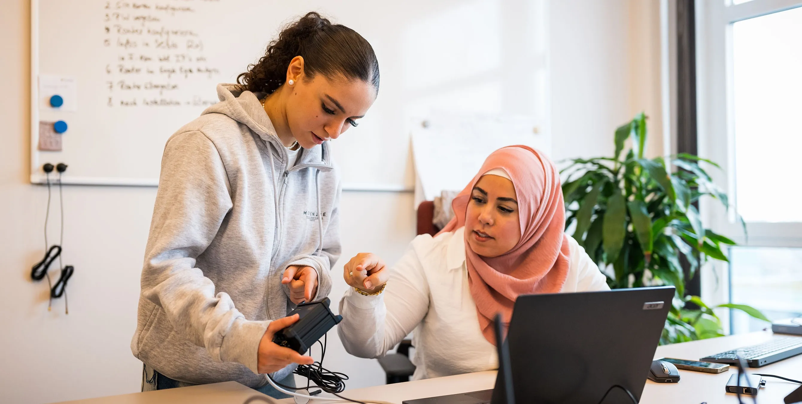 Zwei Frauen an einem Büro-Arbeitsplatz sprechen über ein technisches Gerät, das eine der beiden in der Hand hält. Foto: City-Press GmbH