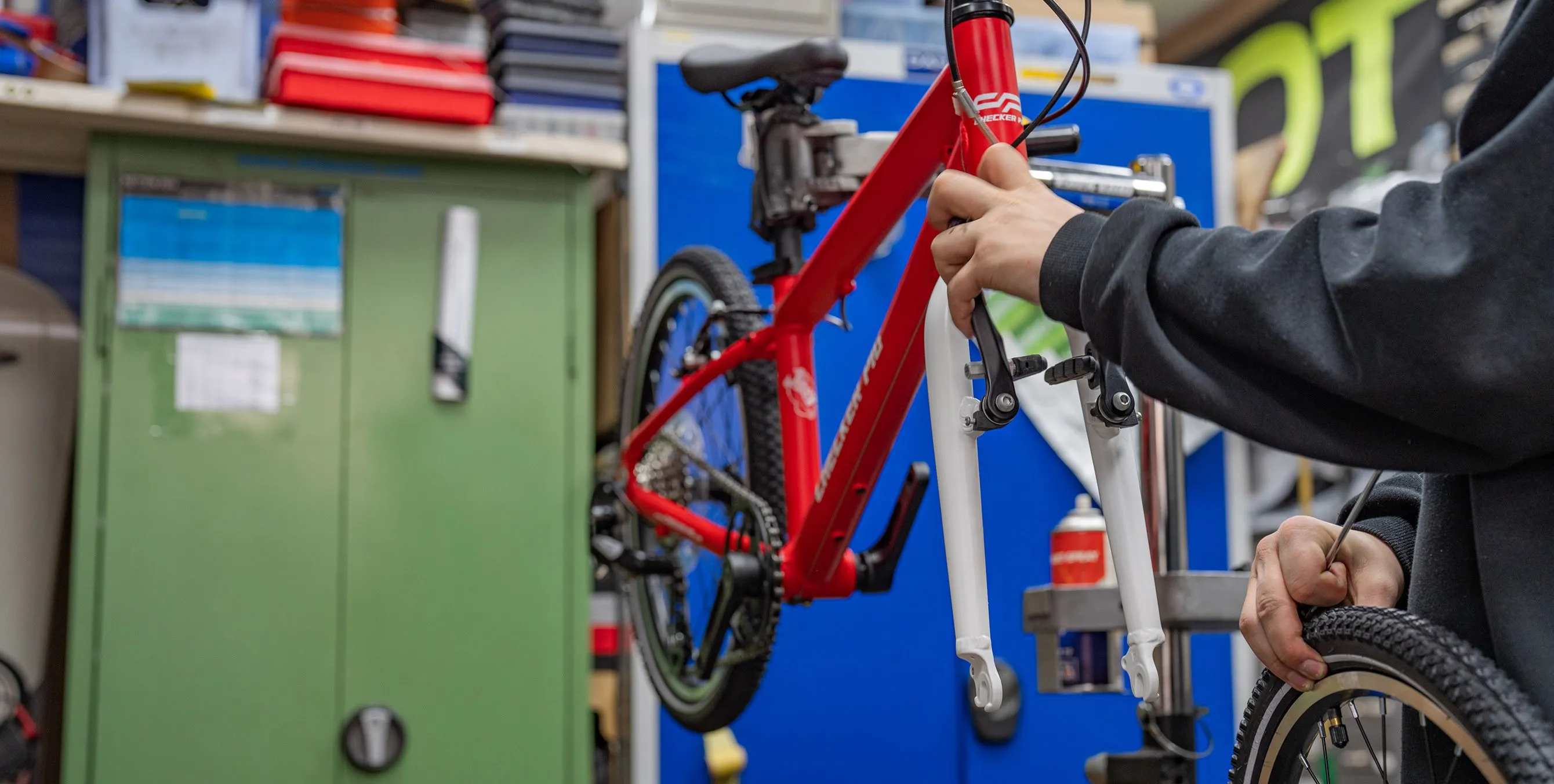 Großaufnahme: Ein rotes Kinderfahrrad hängt in einem Stativ. Davor steht eine Person, die dabei ist, das Laufrad einzusetzen. Foto: Felix Seyfert
