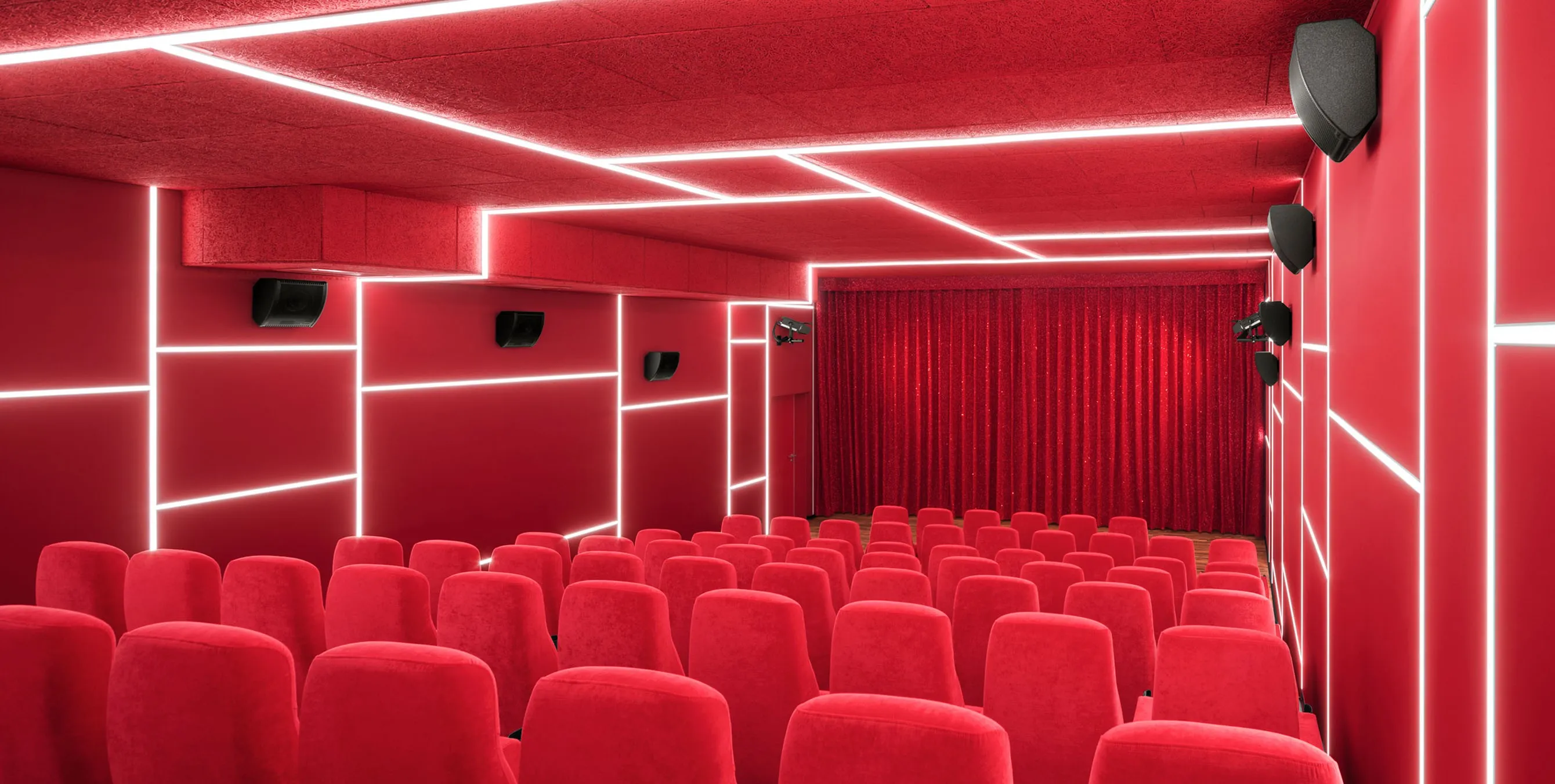 Ansicht von hinten: Ein kleiner, menschenleerer Kinosaal mit roten Sitzen, roten Wänden und rotem Vorhang vor der Leinwand. In die Wände sind markante Lichtleisten eingelassen. Foto: Yorck Kinogruppe/Daniel Horn