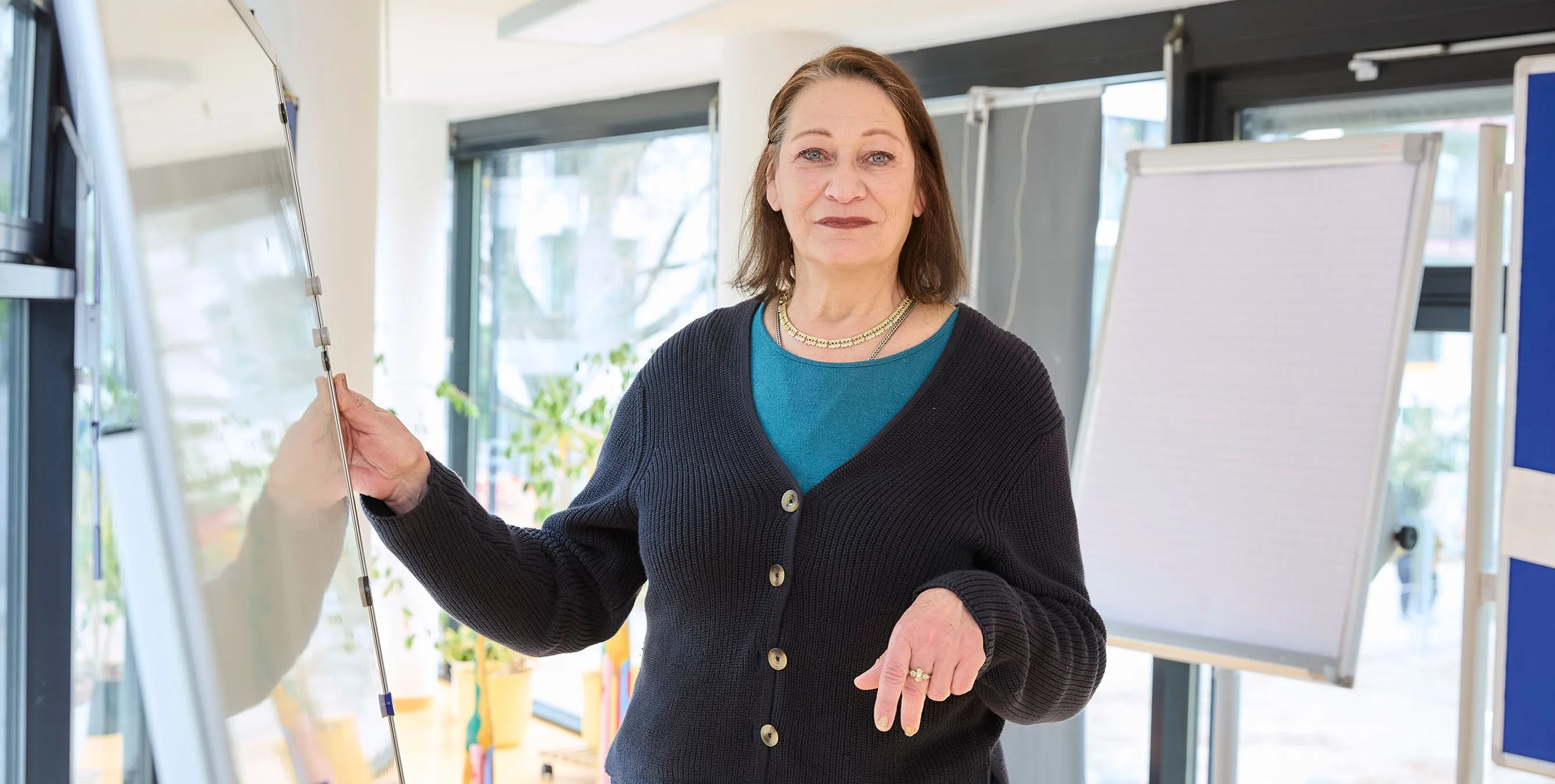 Eine Frau steht an einem Whiteboard und schaut in die Kamera. Im Hintergrund ist ein Flipchart zu sehen. Foto: Britta Leuermann