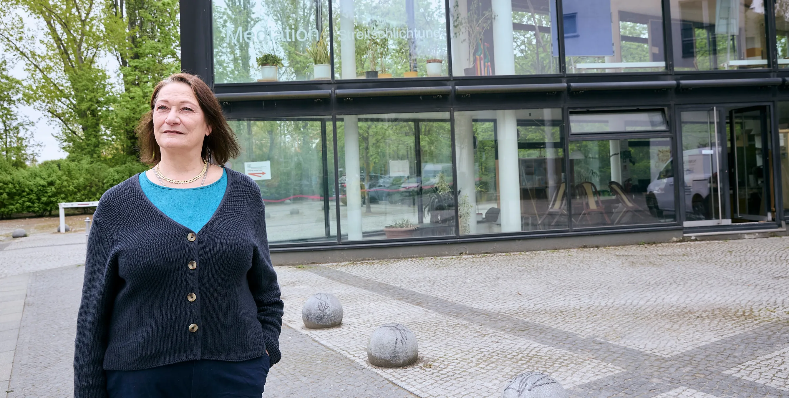Eine Frau steht vor einem gländernen Gebäude. Auf einer Fensterscheibe ist in großen Buchstaben das Wort "Mediation" zu sehen. Foto: Britta Leuermann