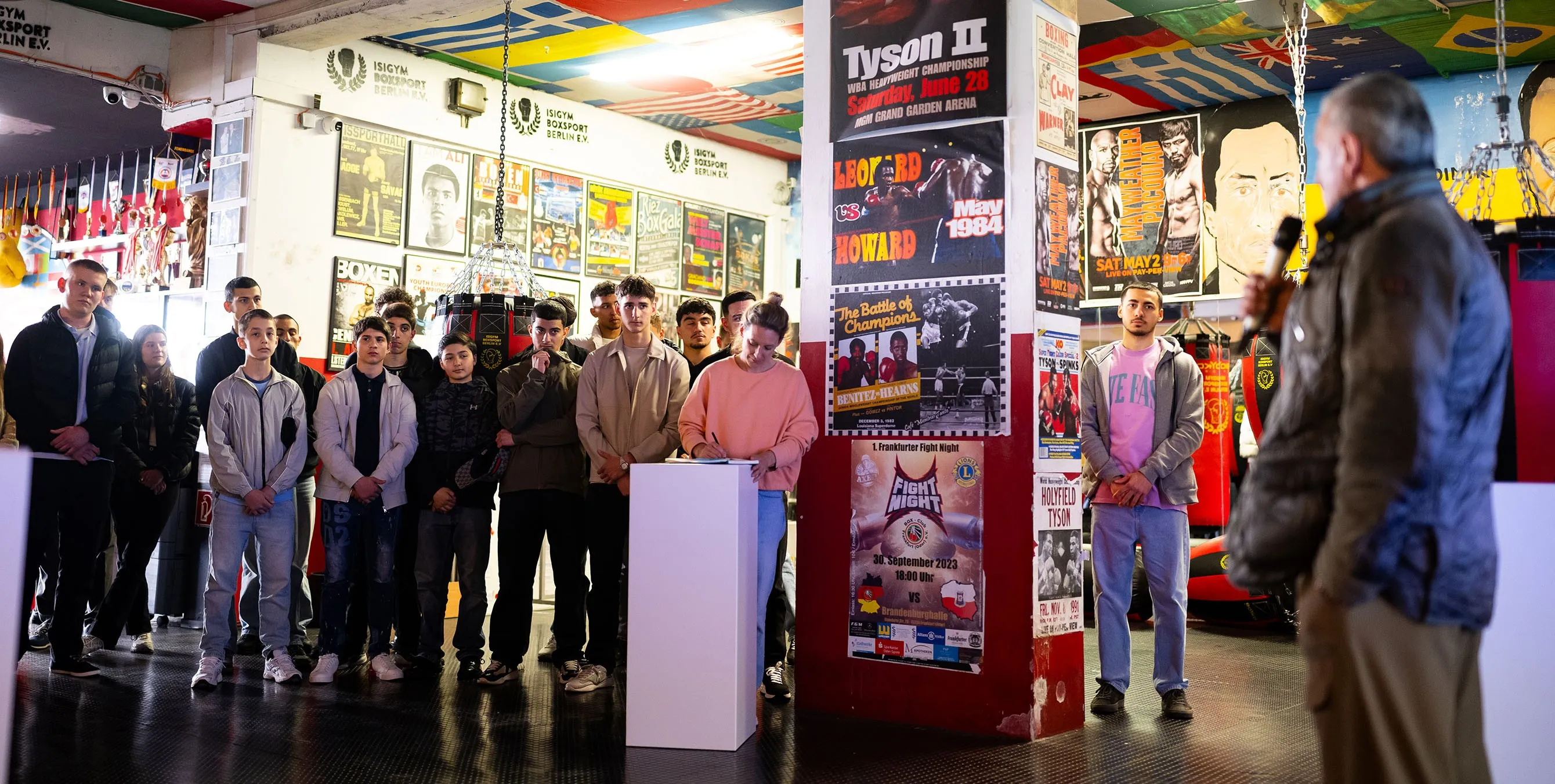 In einem Boxgym stehen mehrere Jugendliche im Halbkreis und hören einer Rede zu. Foto: City-Press GmbH