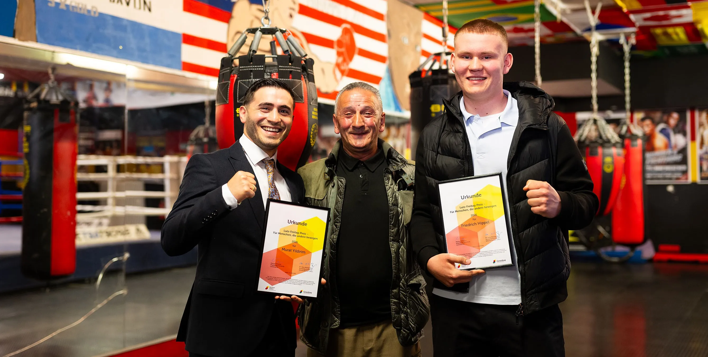 Zwei junge Männer halten jeweils gerahmte Urkunden, machen mit der zweiten Hand eine Faust und lächeln in die Kamera. Zwischen ihnen steht einer älterer Trainer, der lächelt. Foto: City-Press GmbH