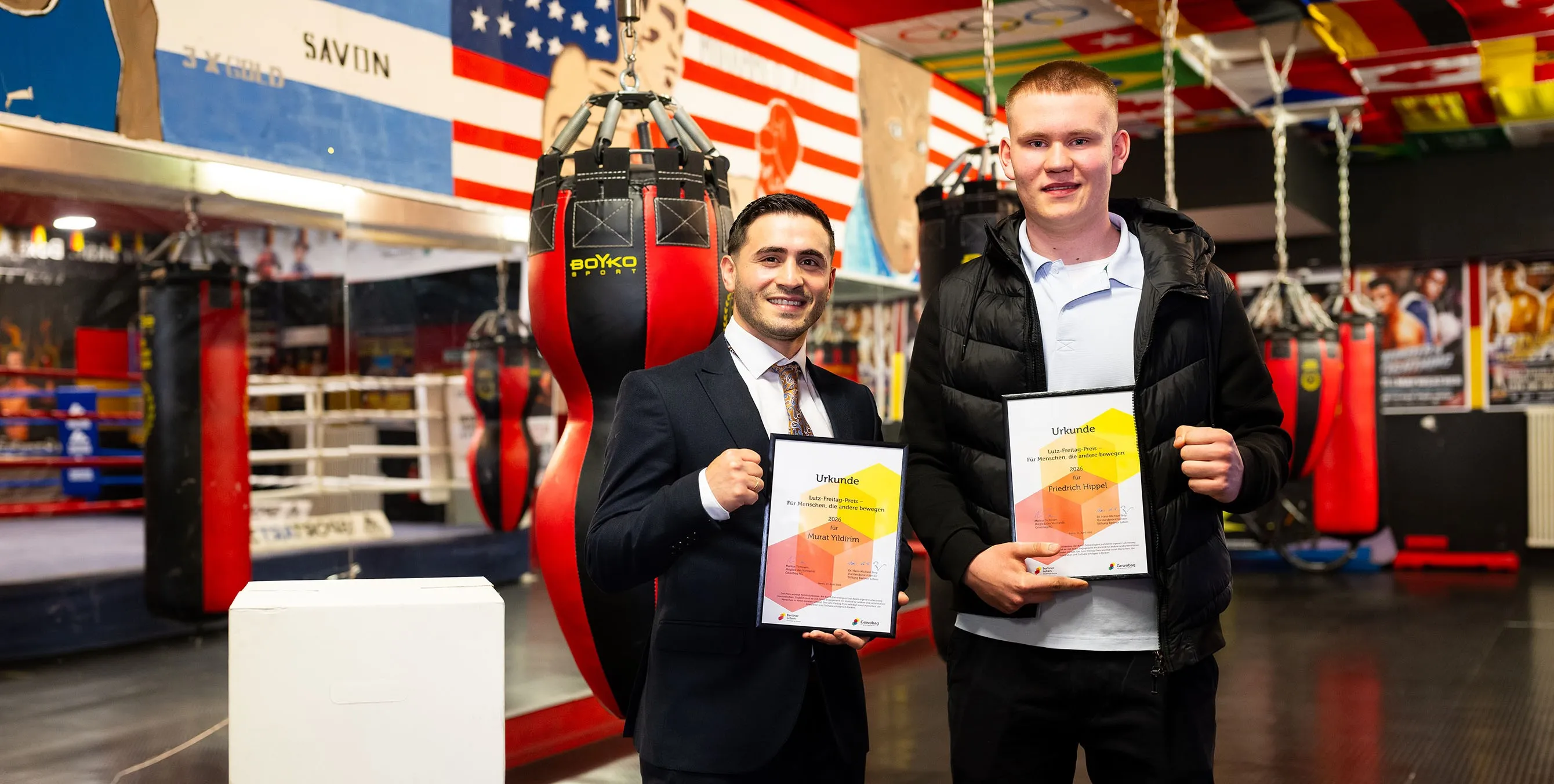 Zwei junge Männer halten jeweils gerahmte Urkunden, machen mit der zweiten Hand eine Faust und lächeln in die Kamera. Foto: City-Press GmbH