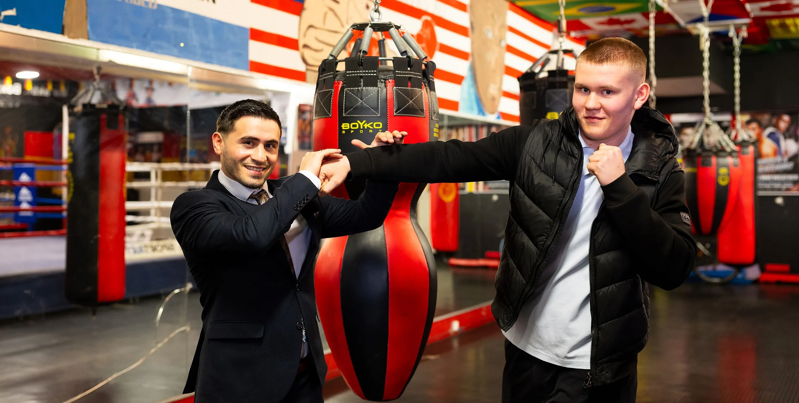 Zwei junge Männer stehen in einem Boxgym und simulieren eine Szene aus einem Boxkampf. Dabei lächeln sie in die Kamera. Foto: City-Press GmbH