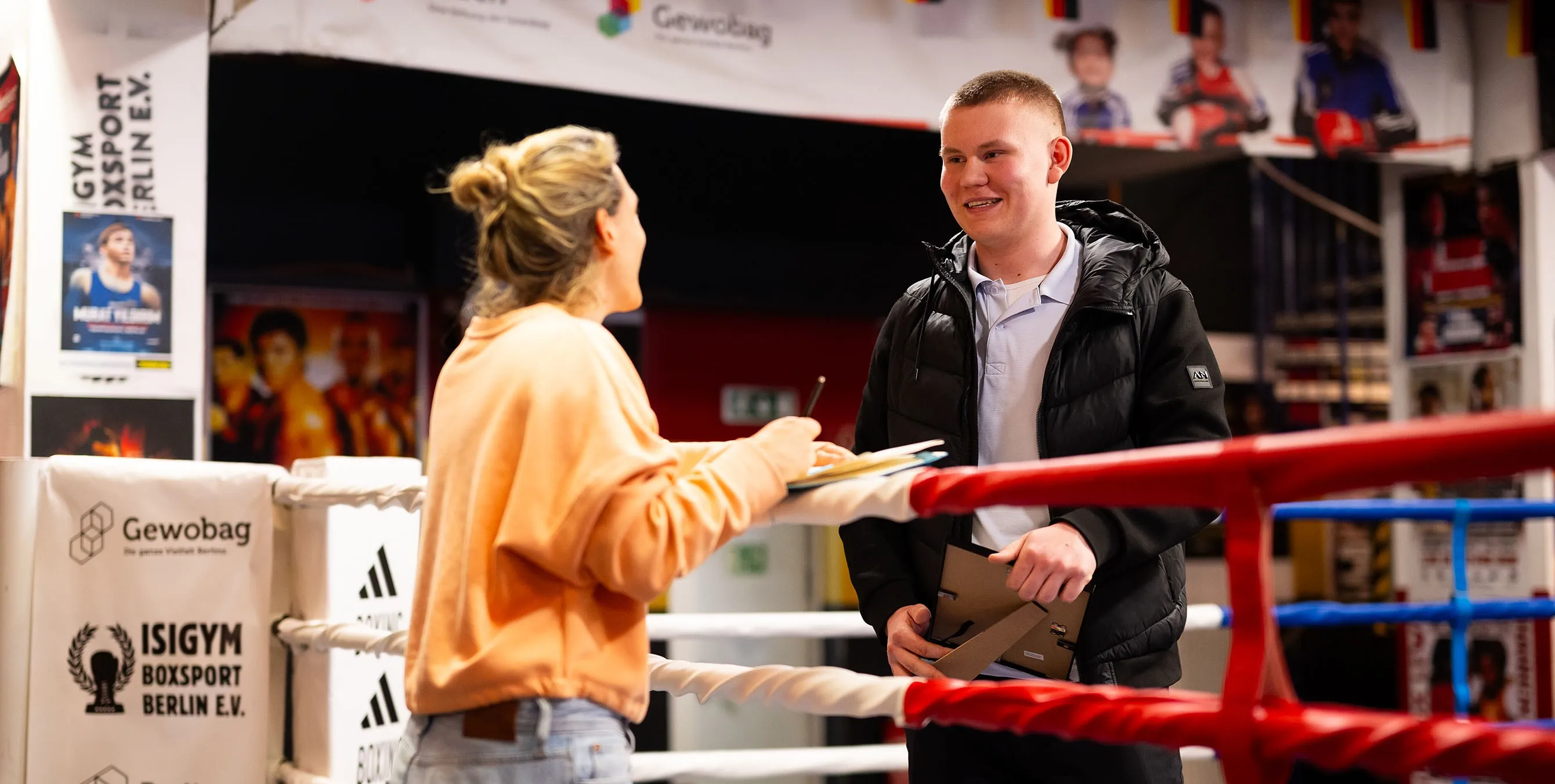 Ein junger Mann steht in einem Boxgym und unterhält sich über die Ringseile hinweg mit einer Reporterin. Foto: City-Press GmbH