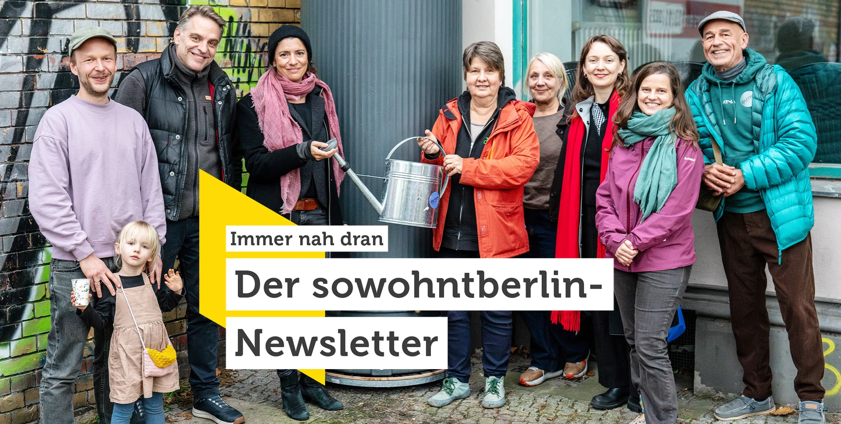 Personengruppe steht vor einem Haus mit Regentonne