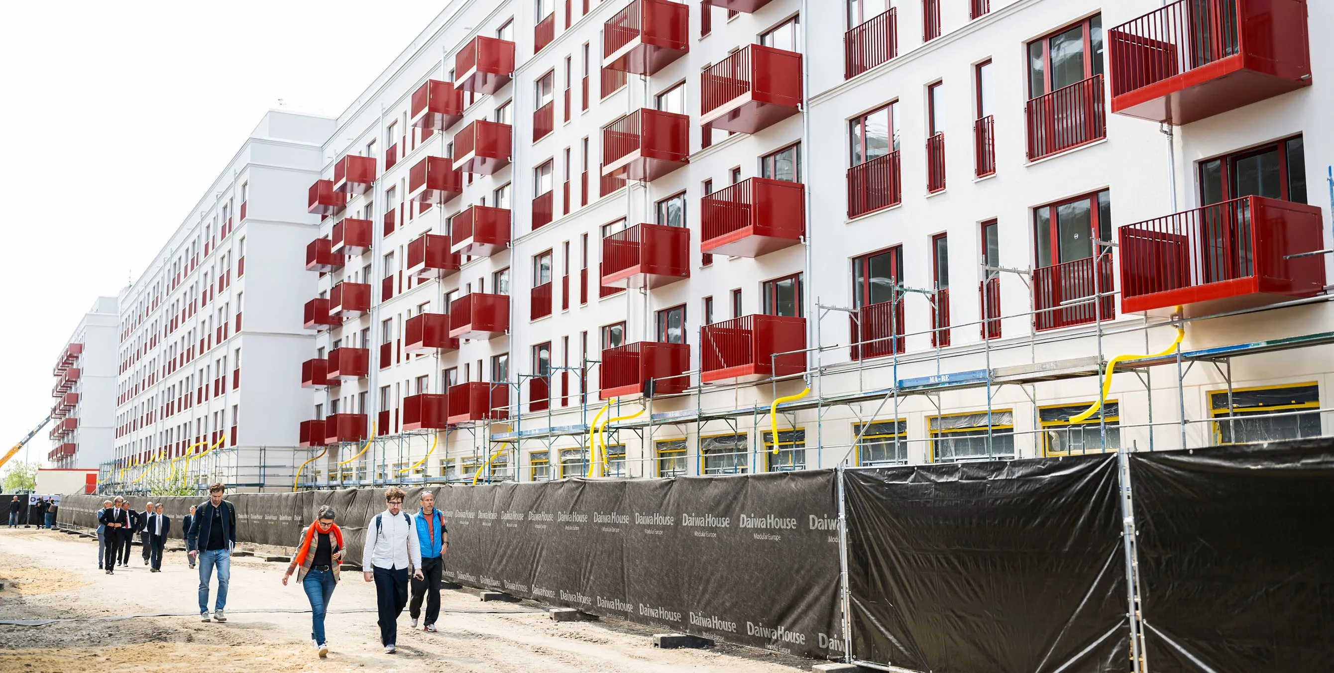 Aufnahme von der Seite: Ein langgezogener, weißer Neubau mit knallroten Fenstergittern und Balkonen. Foto: City-Press GmbH