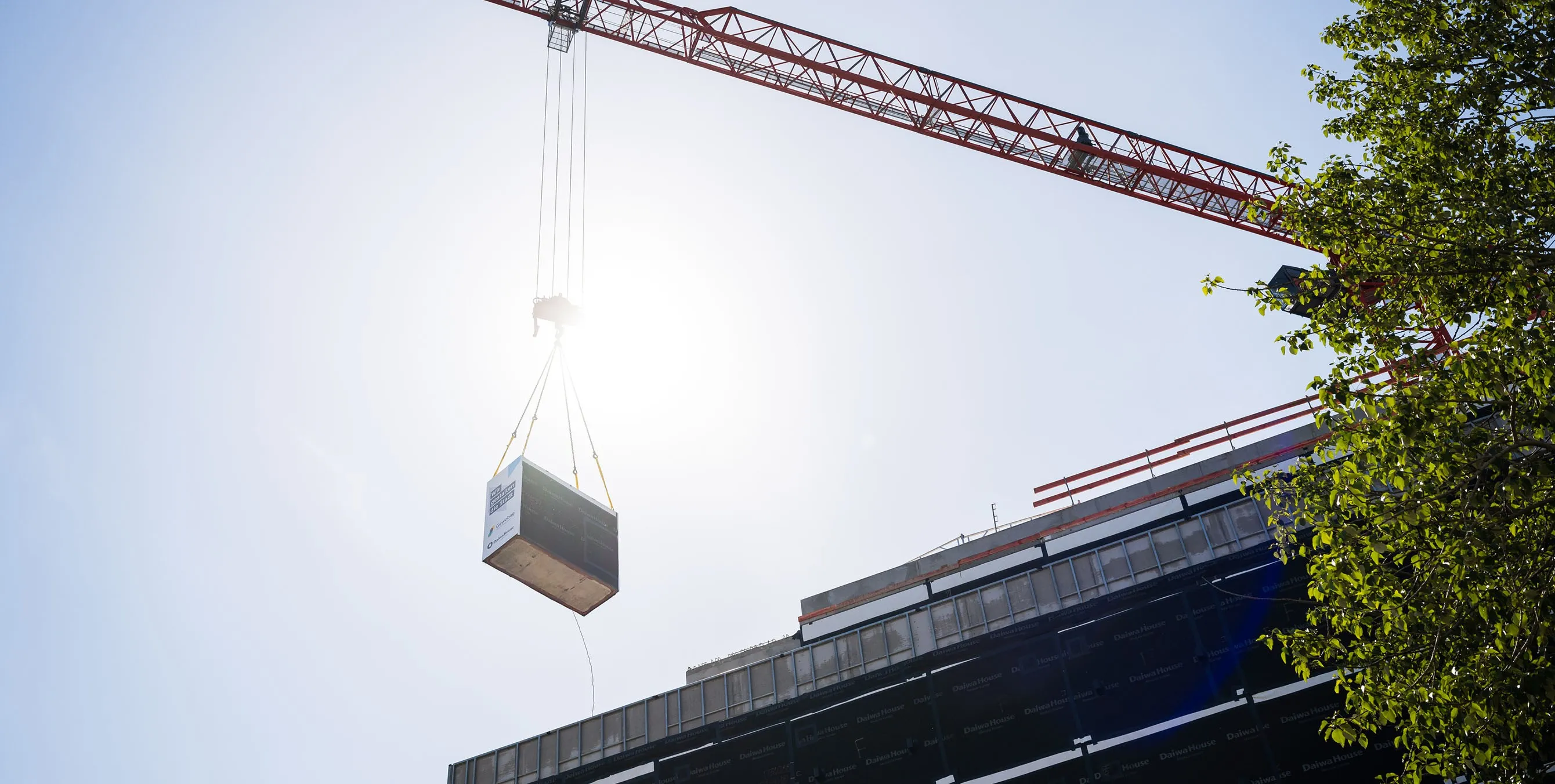 Ein containerartiges Wohnungsbaumodul wird an einem Kran in die Höhe gezogen und auf ein Gebäude gesetzt. Foto: City-Press GmbH