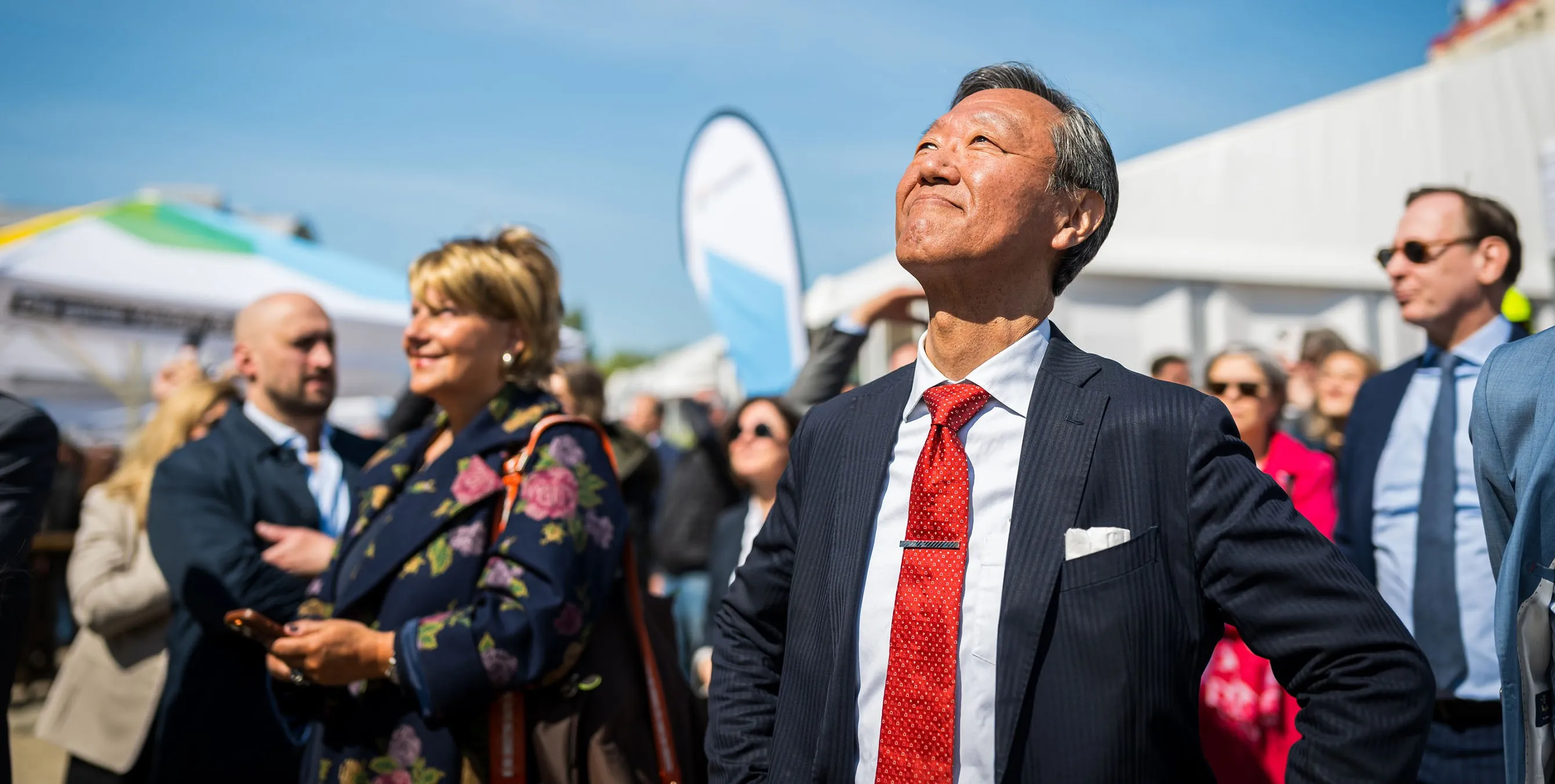 Ein asiatischer Mann im Anzug steht im Freien und schaut bei einem Event lächelnd gen Himmel. Foto: City-Press GmbH
