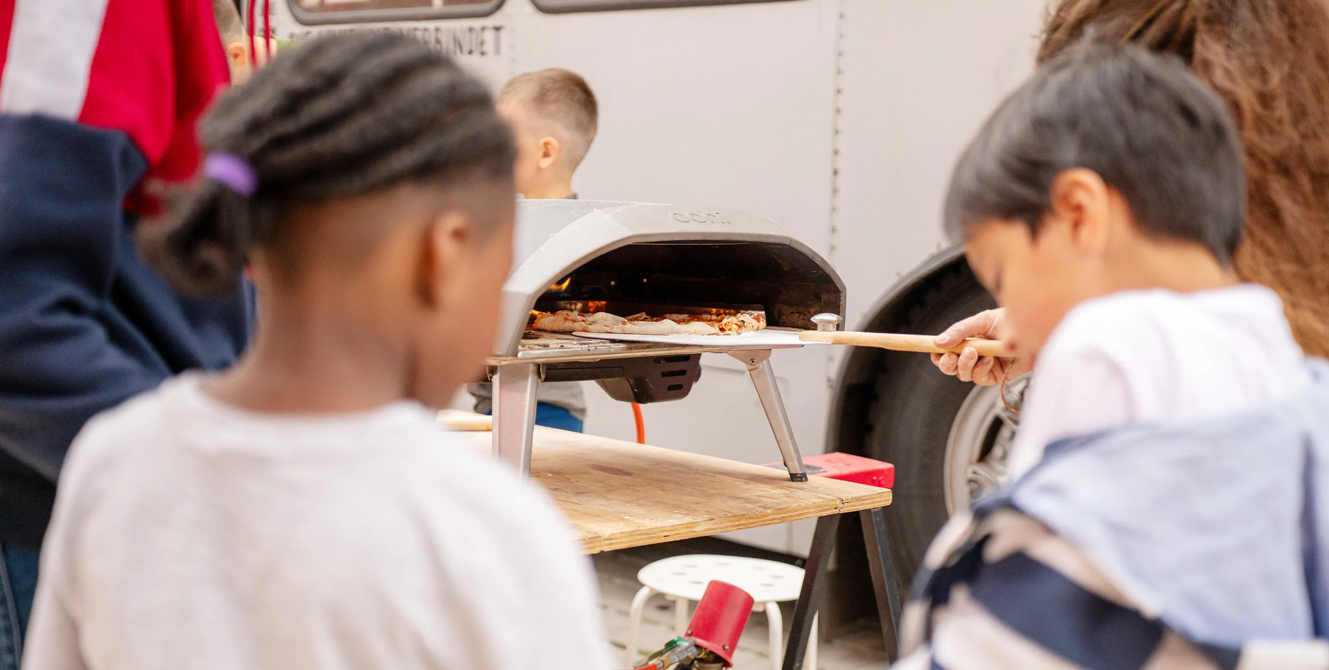 Großaufnahme: Eine Person schiebt bei einem Nachbarschaftsfest eine Pizza in einem mobilen Pizzaofen. Foto: Ralph Maak