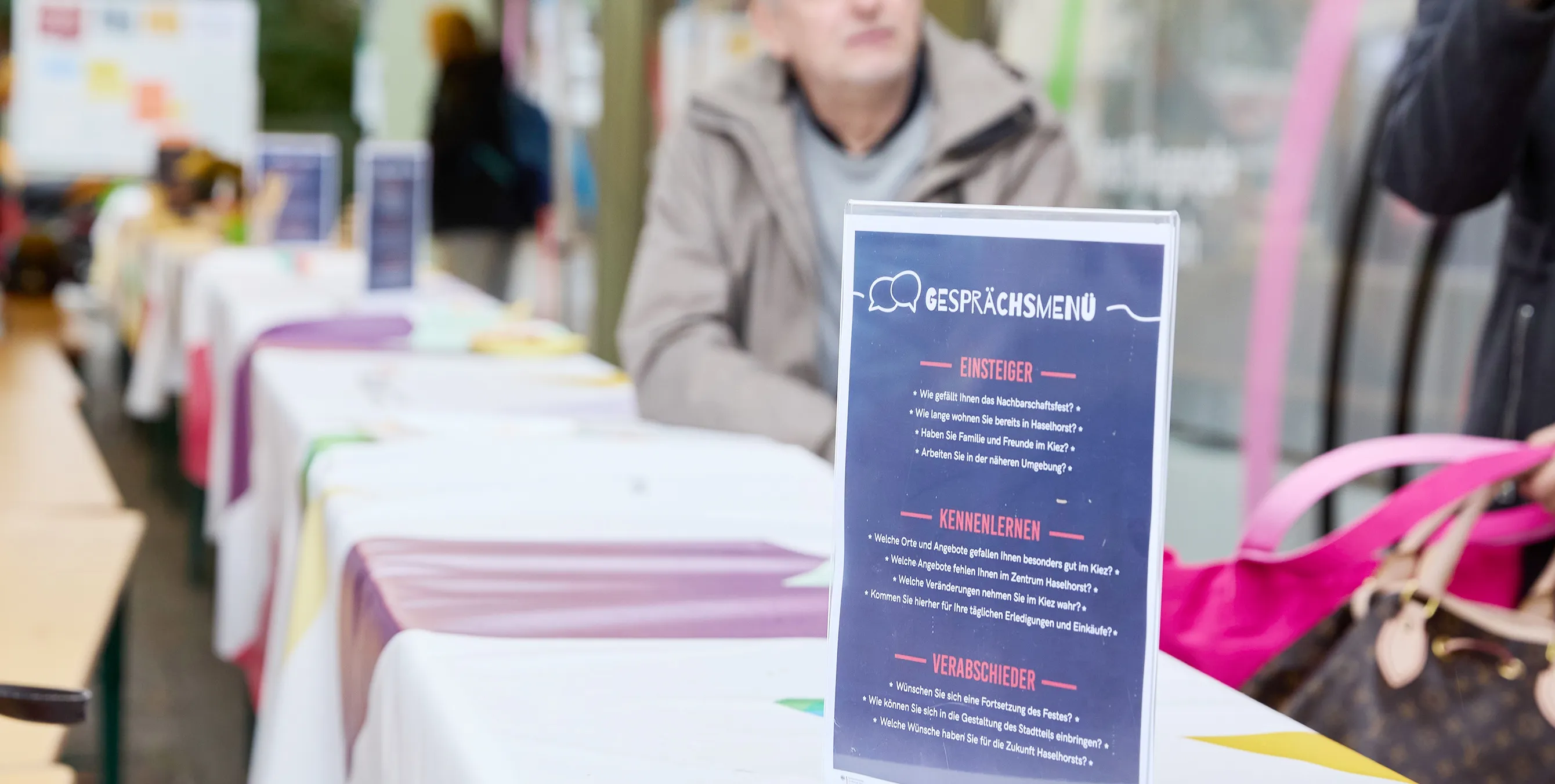 Eine lange Tafel mit bunter Tischdecke, darauf ein Aufsteller mit dem Aufschrift "Gesprächsmenü" und diversen Fragen, um ein Gespräch zu beginnen. Foto: Britta Leuermann