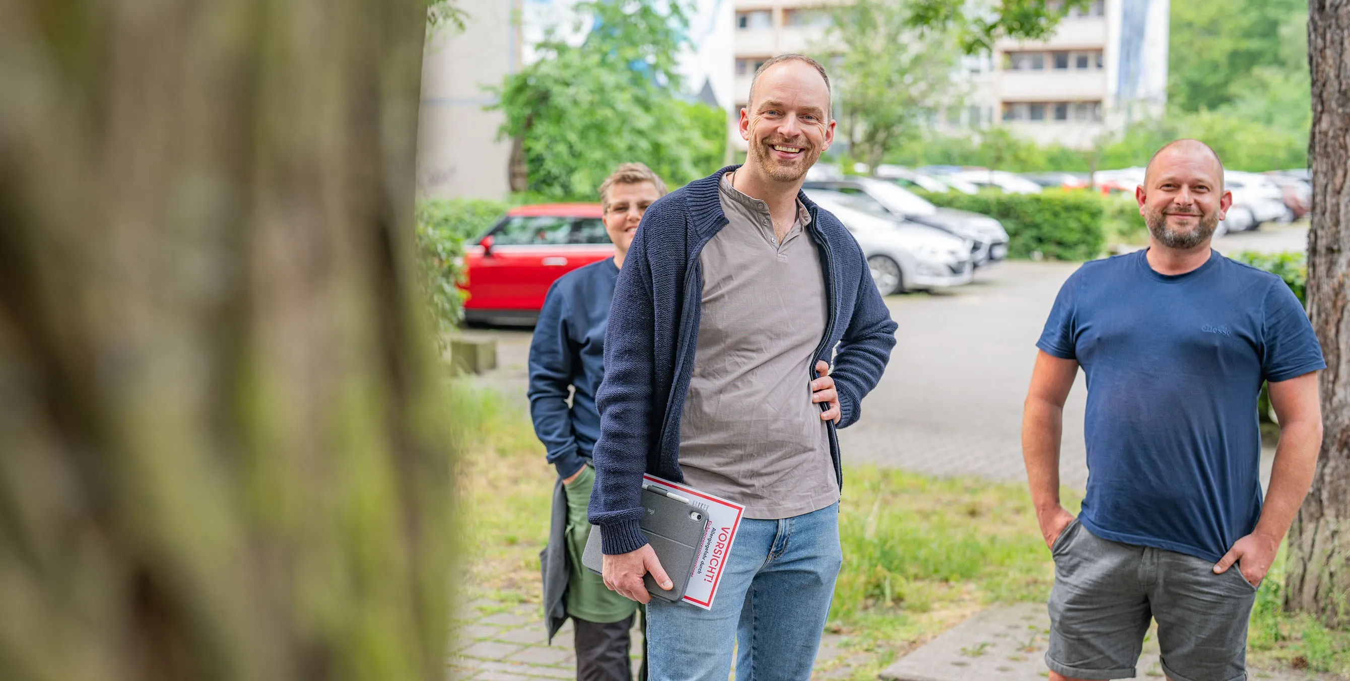 Drei Personen stehen in einem Wohnquartier und lächeln in Richtung Kamera. Im Anschnitt ist ein Baum zu erkennen. Foto: Felix Seyfert