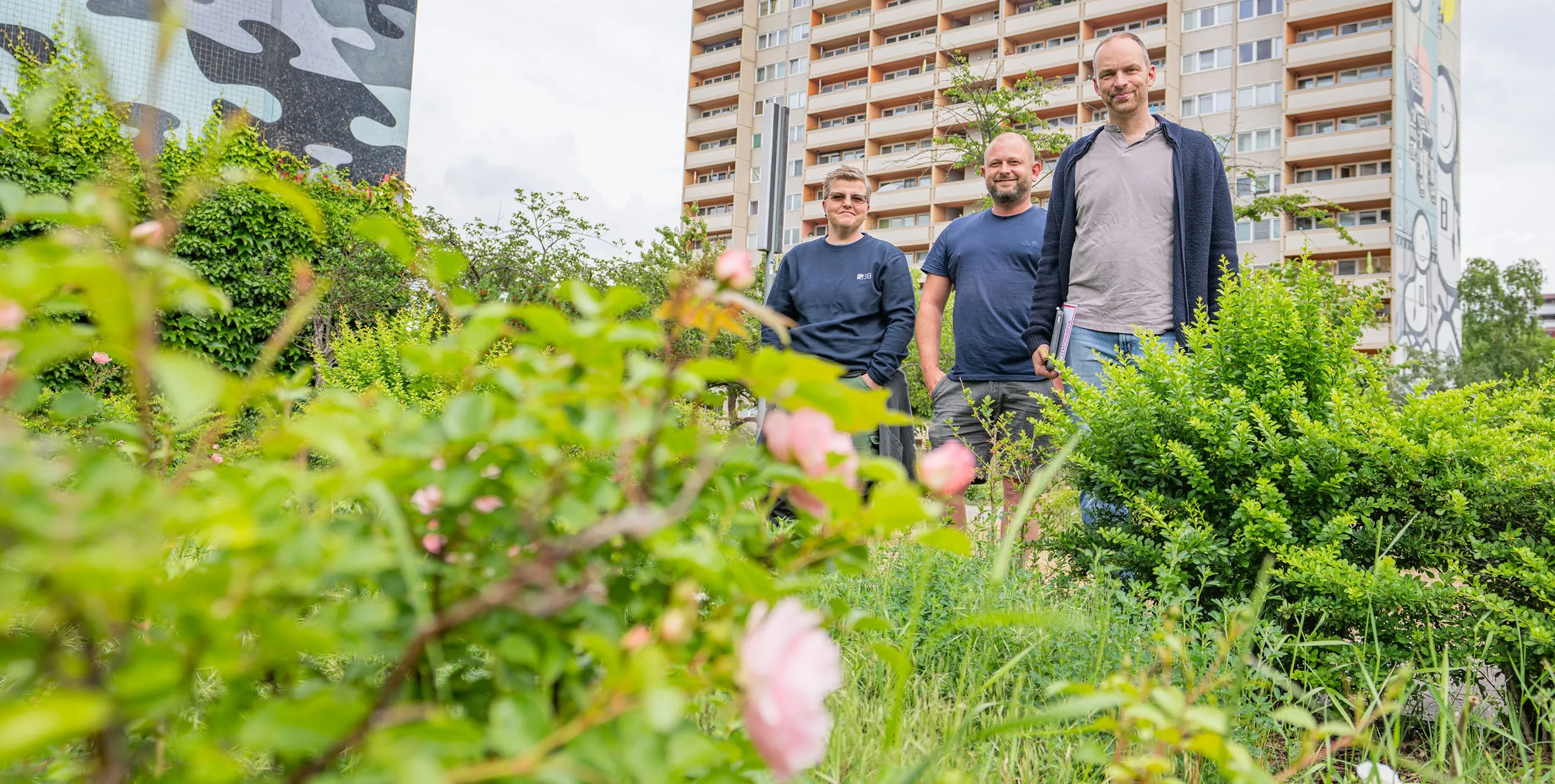 Drei Personen stehen umringt von diversen Pflanzen in einem Wohnquartier. Im Hintergrund sind große Mehrfamilienhäuser zu sehen. Foto: Felix Seyfert