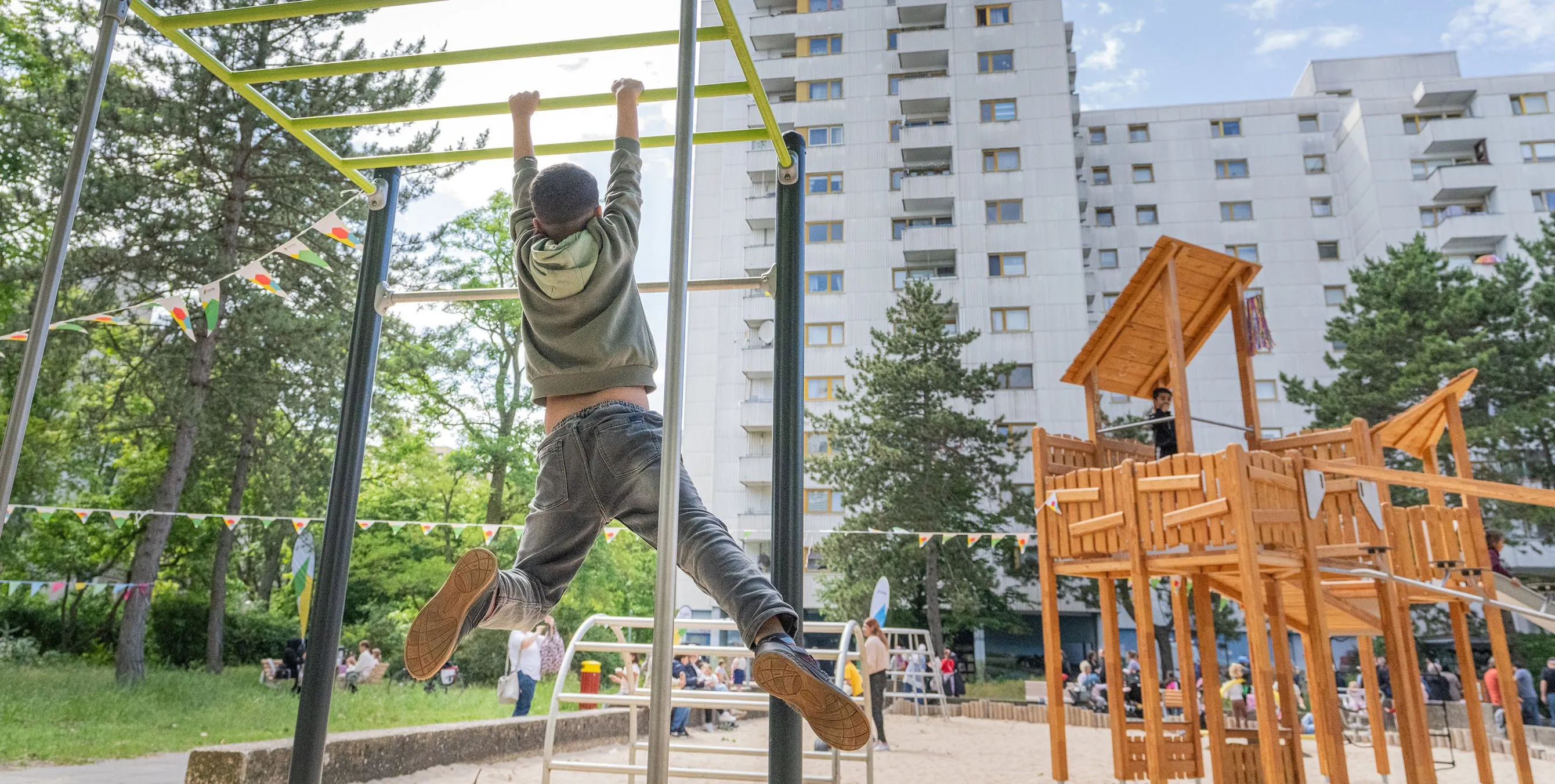 Ein Kind hangelt an einem Spielgerät auf einem Spielplatz im Freien. Im Hintergrund ist ein großes Mehrfamilienwohnhaus zu sehen. Foto: Felix Seyfert