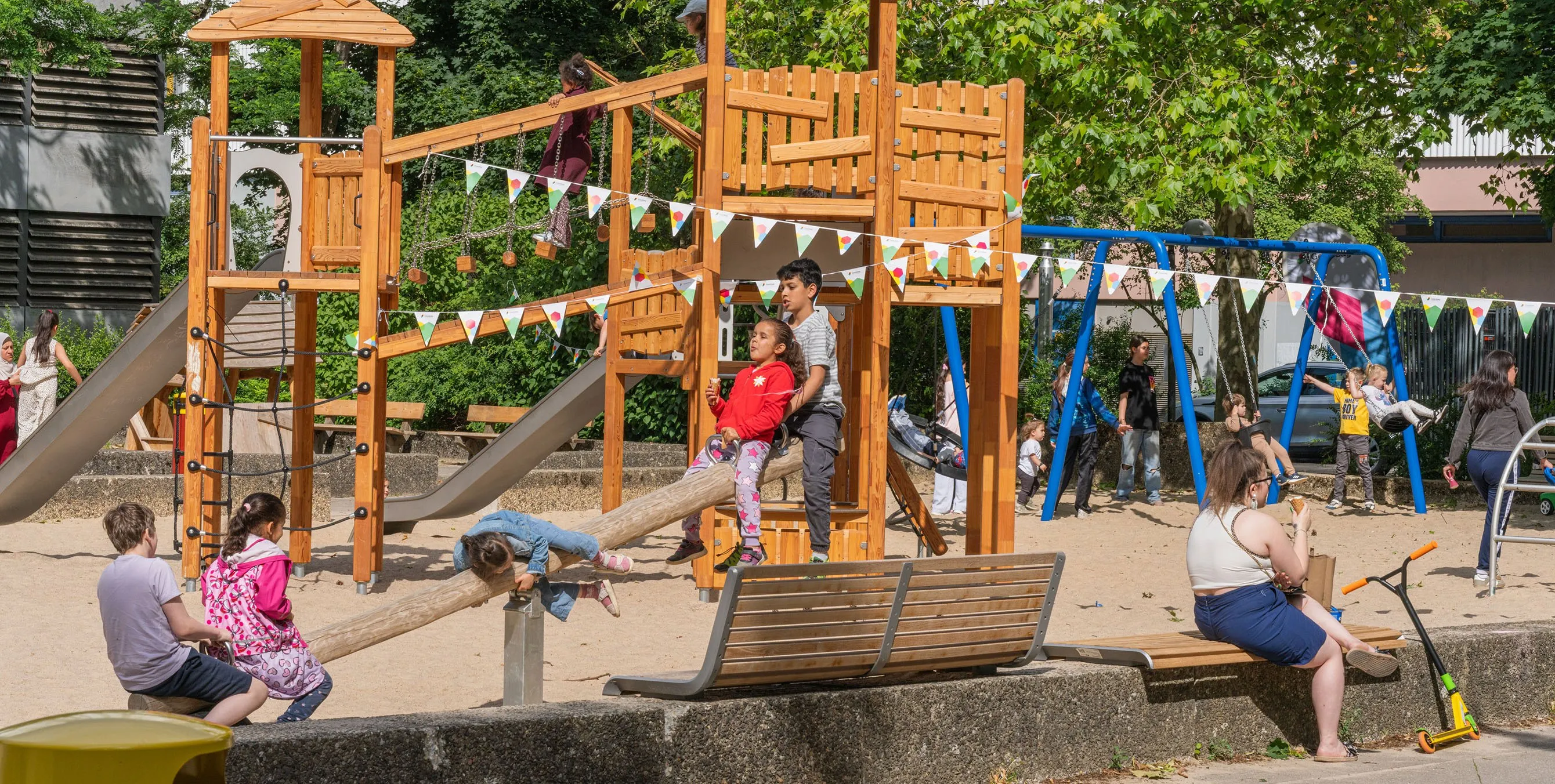 Spielende Kinder auf einem Spielplatz mit neuem, großen Spielgerät, an dem Wimpelketten befestigt sind. Foto: Felix Seyfert