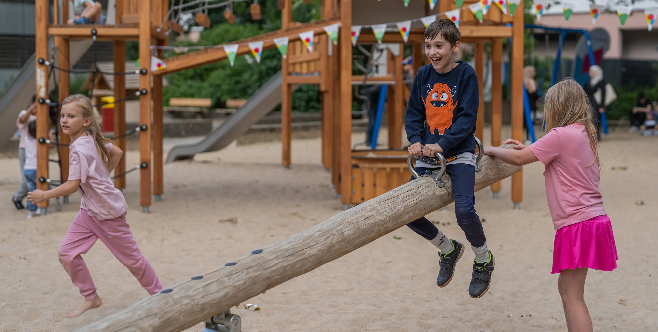 Kinder spielen auf einem Spielplatz an einer Wippe. Im Hintergrund ist eine Wimpelkette zu sehen. Foto: Felix Seyfert