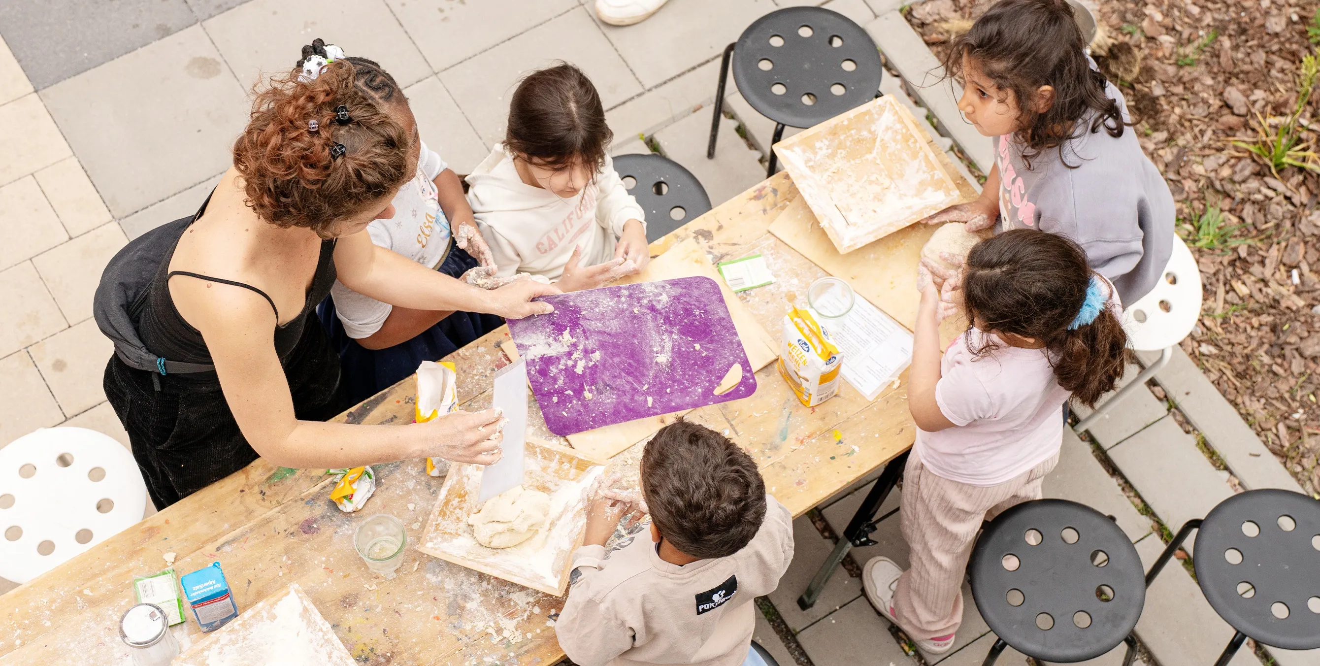 Aufnahme aus der Vogelperspektive: Kinder an einem Tisch im Freien beim Zubereiten von Pizza. Foto: Ralph Maak