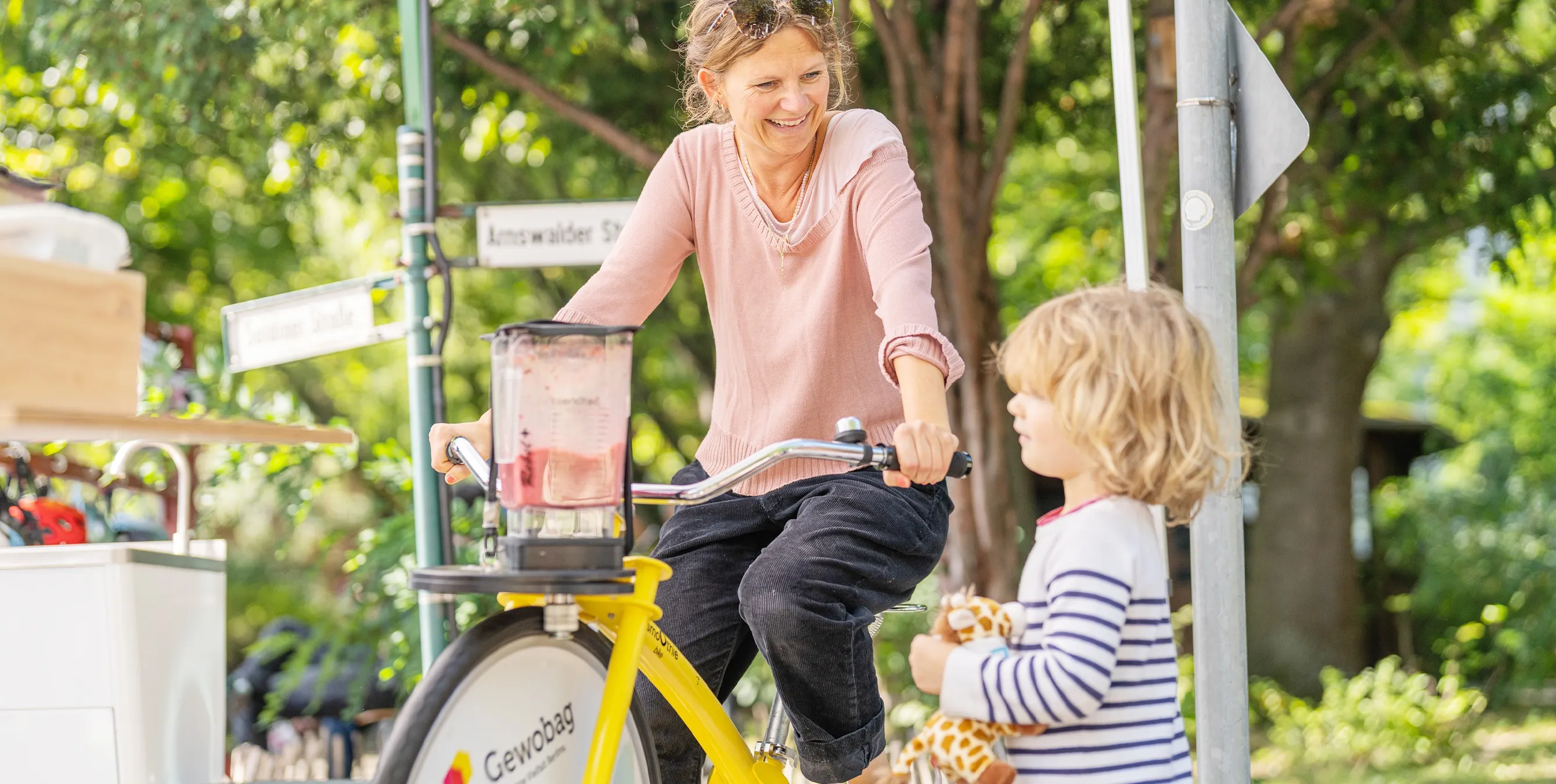 Eine Frau sitzt auf einem Smoothie Bike und lacht. Davor steht ein Kind und schaut zu. Foto: Felix Seyfert