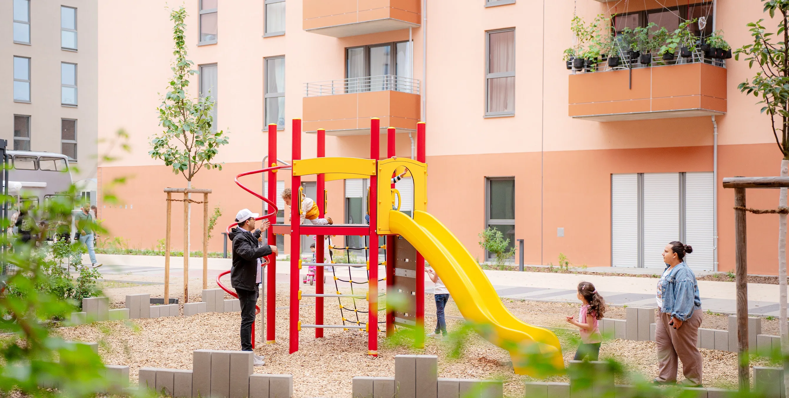Kleine Kinder mit Eltern auf einem Spielgerät mit Rutsche in einem Neubauquartier. Foto: Ralph Maak