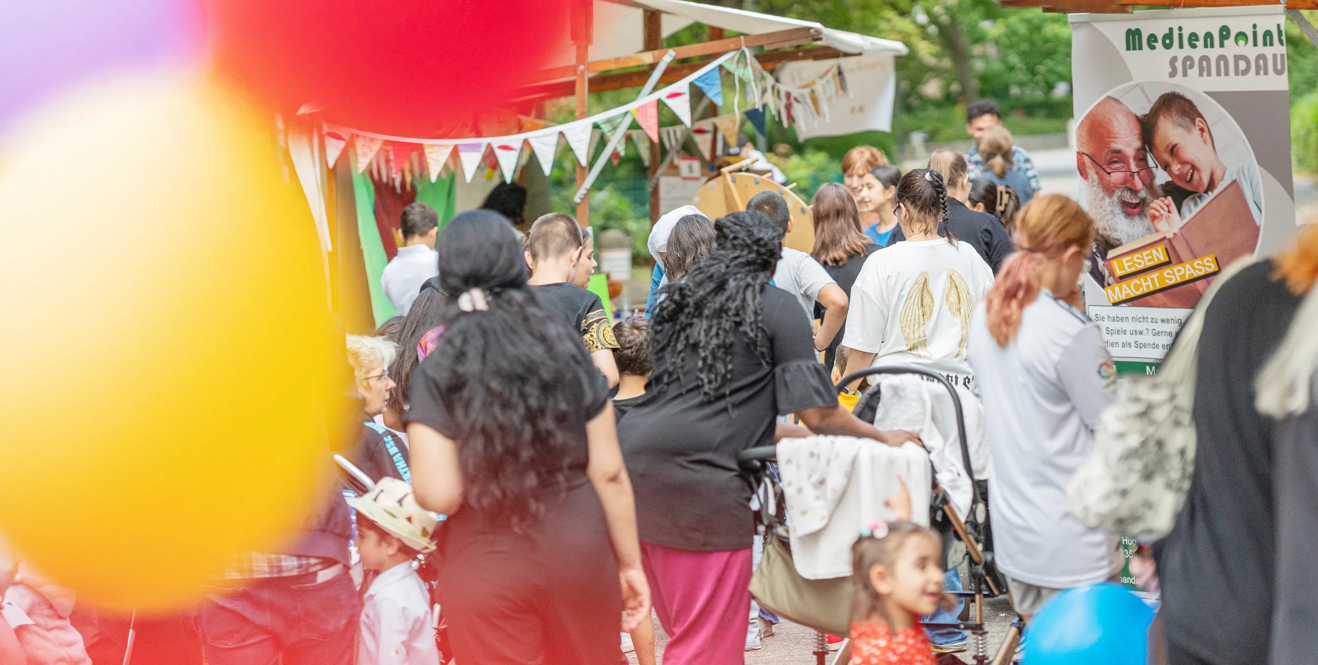Erwachsene und Kinder auf einem Nachbarschaftsfest. Auch Luftballons, eine Stand und Wimpelketten sind zu sehen. Foto: Felix Seyfert